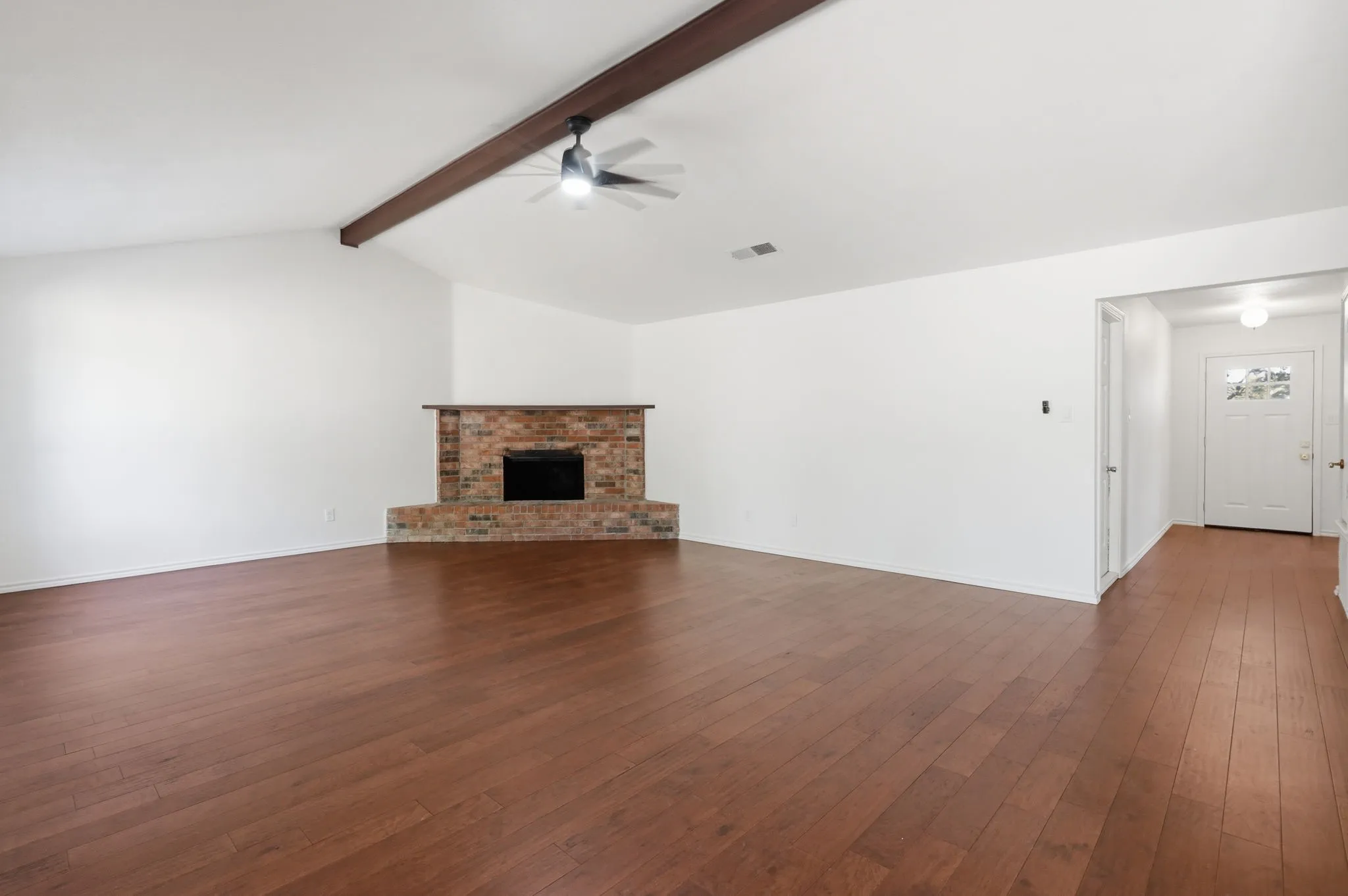 Vaulted ceiling with exposed wood beam, wood-finish flooring, brick fireplace, and ceiling fan
