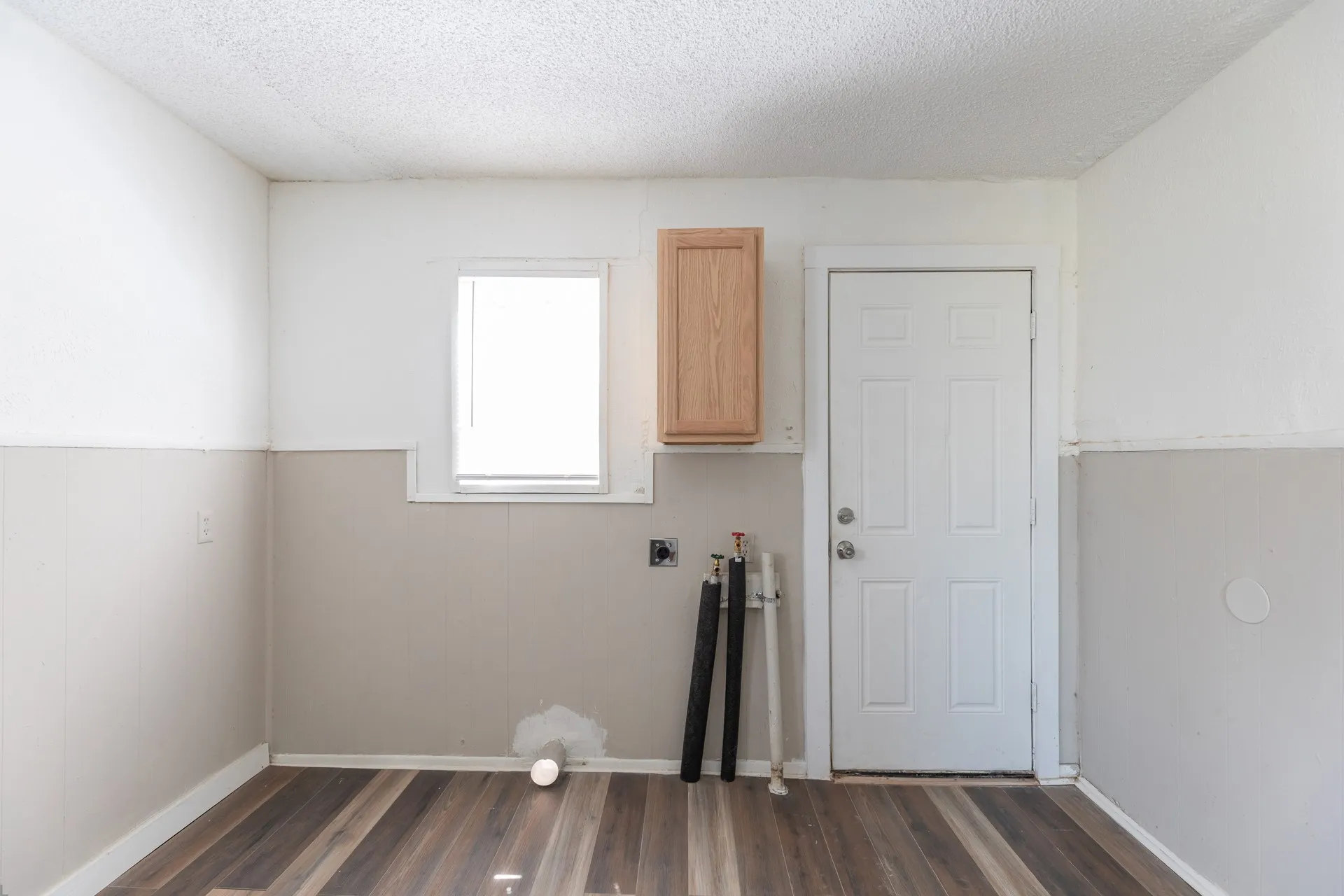 Wood-finish flooring, white paneled door, light wood cabinetry, and a bright window