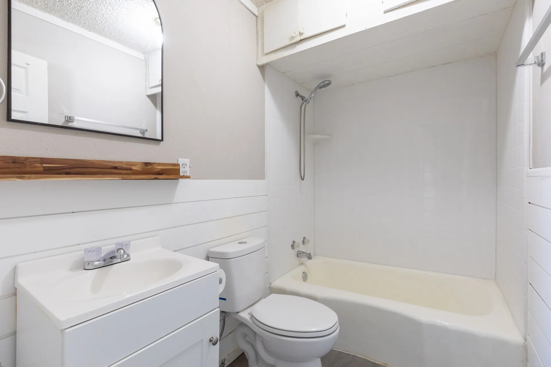 White vanity with integrated sink, wood-finish accent shelf, and a shower-over-tub combination