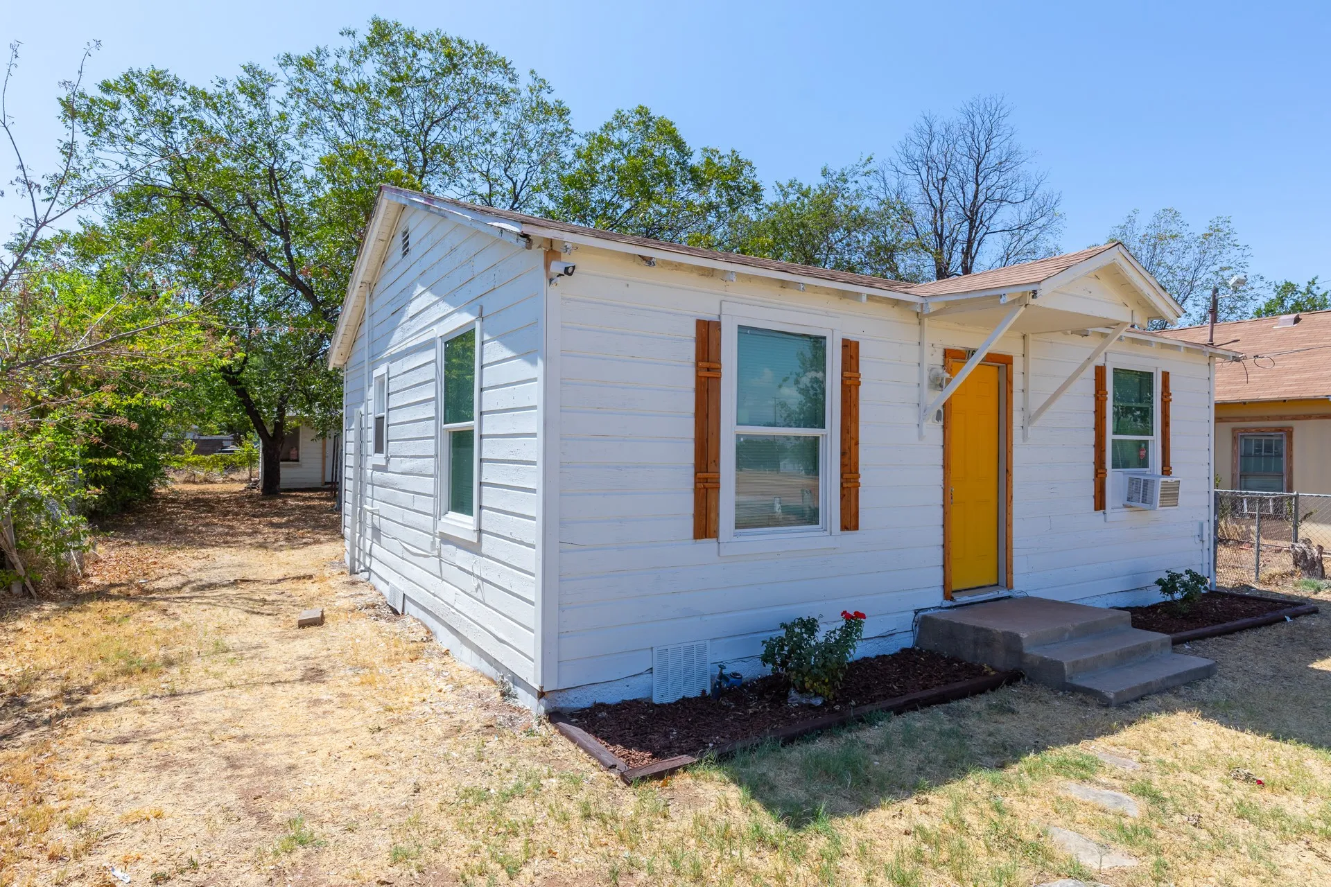 White siding exterior with a bright yellow front door, accented by wood-finish shutters