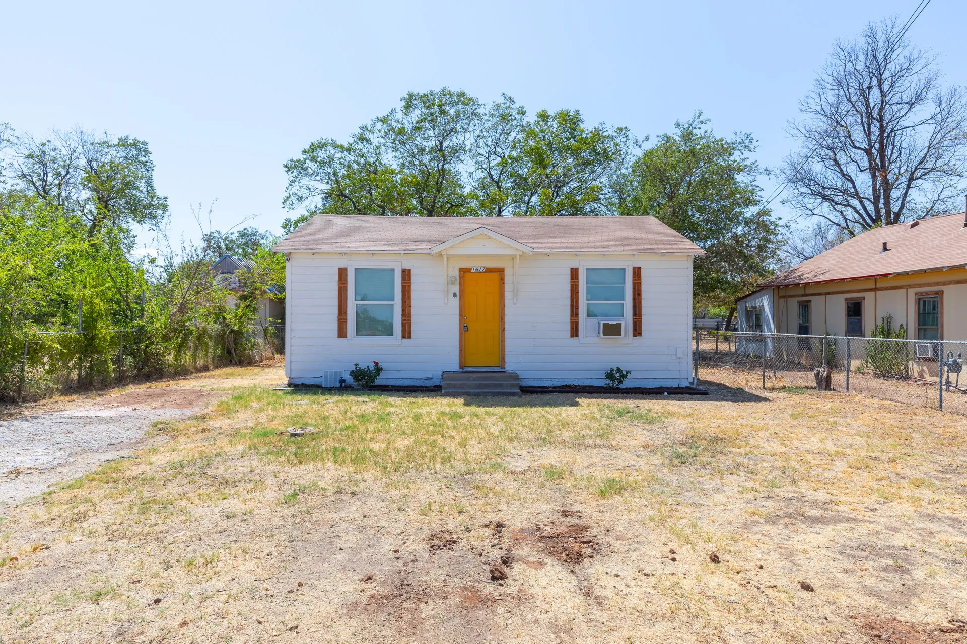 White exterior with a vibrant yellow entry door, framed by decorative shutters