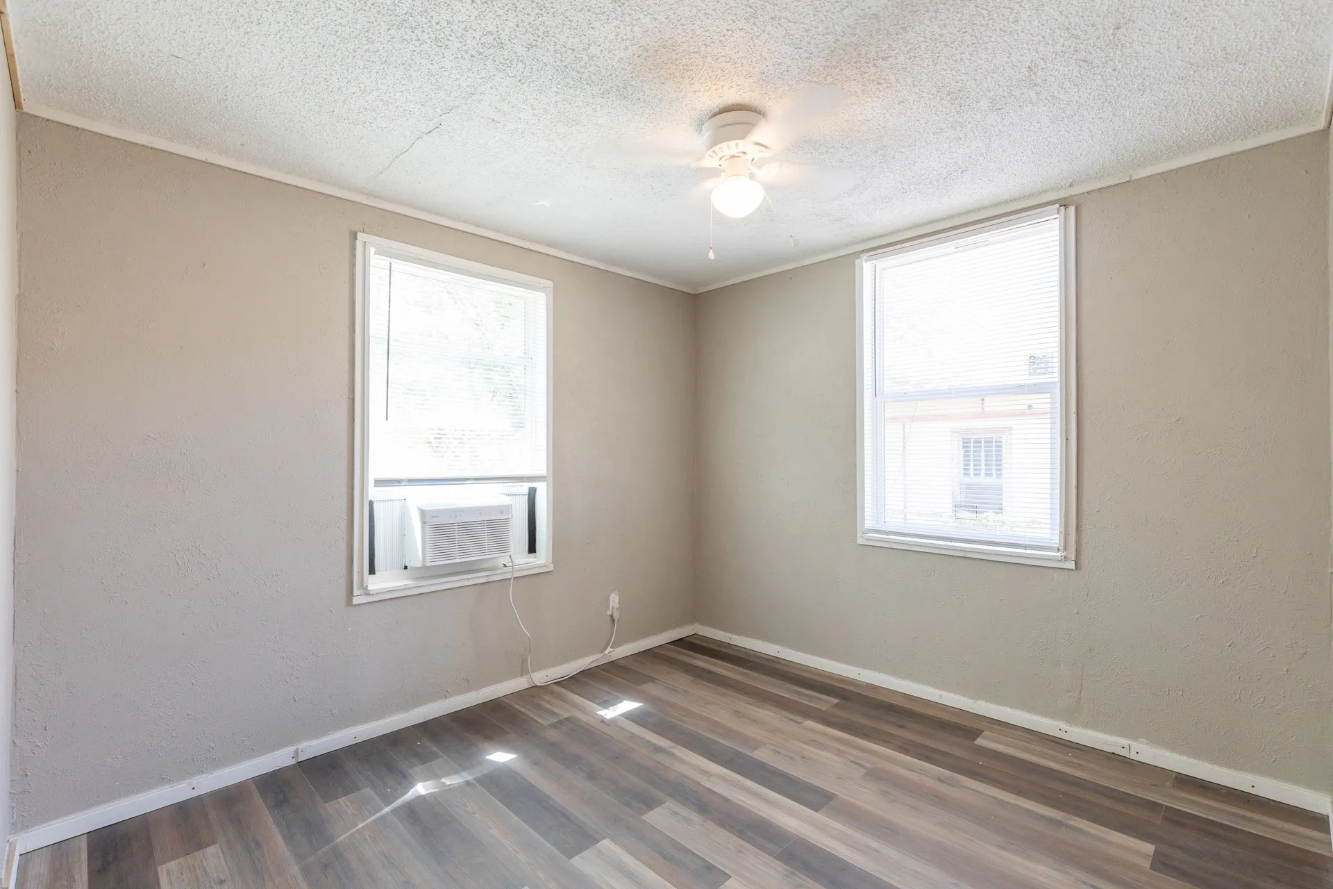 Wood-finish flooring, two windows with blinds, and a ceiling fan with light fixture