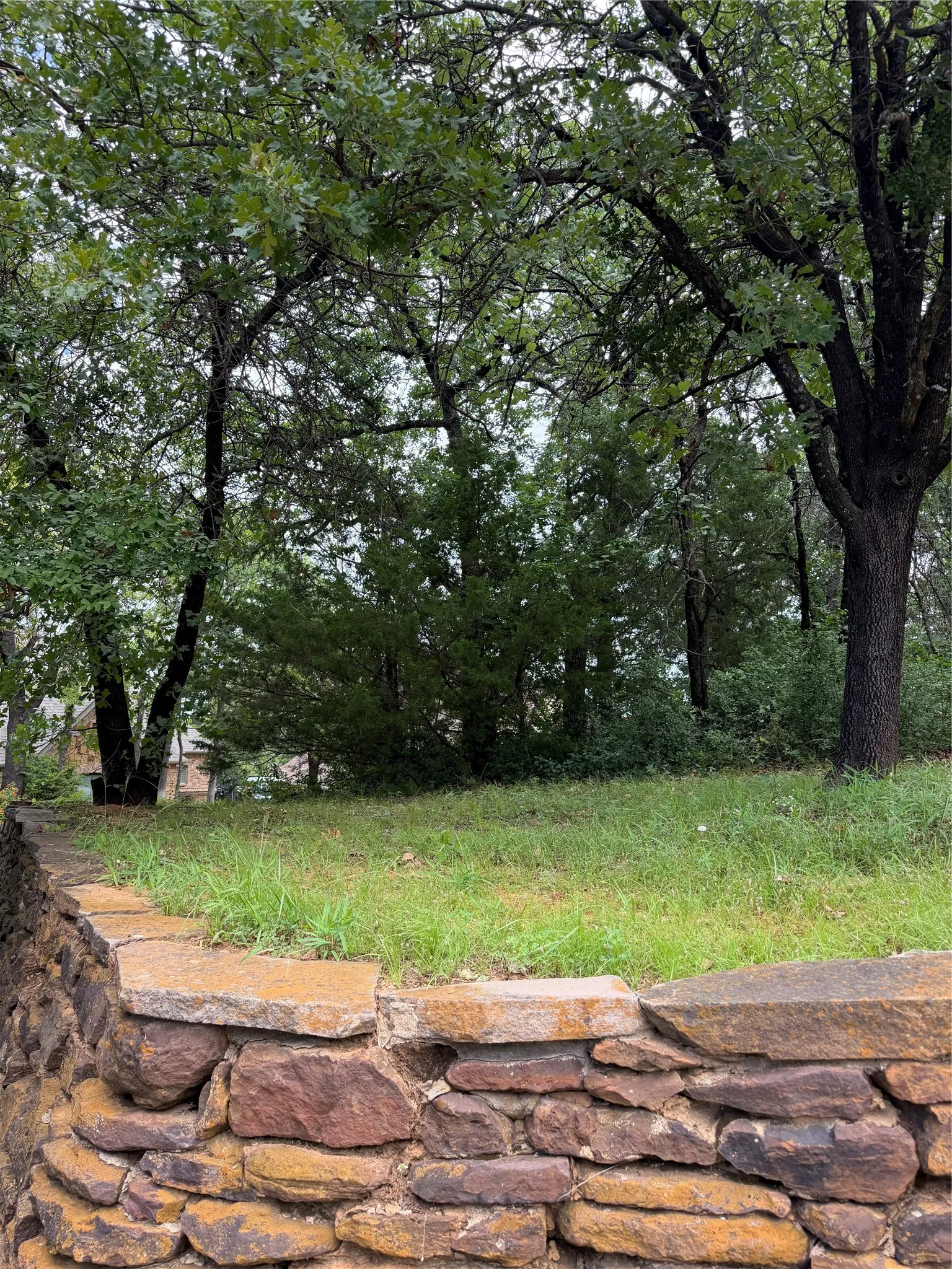 Corner of lot Stacked stone retaining wall with natural capstones and mature trees