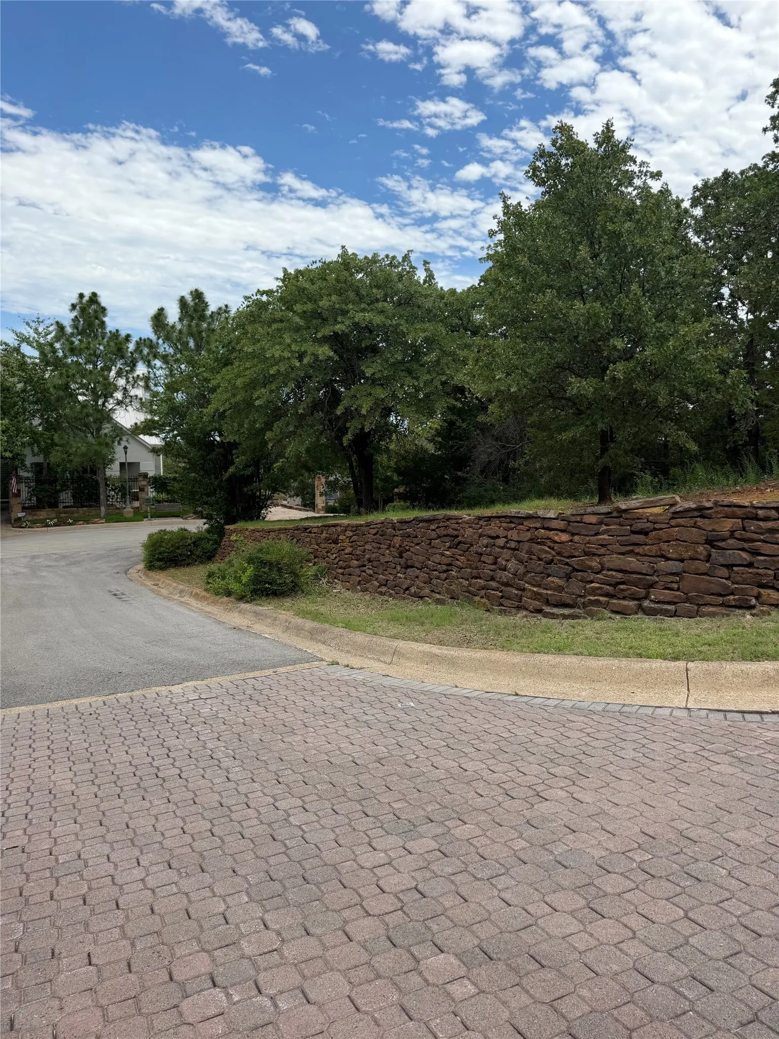 Paver stone street surface, stone retaining wall, mature trees, and landscaped shrubbery
