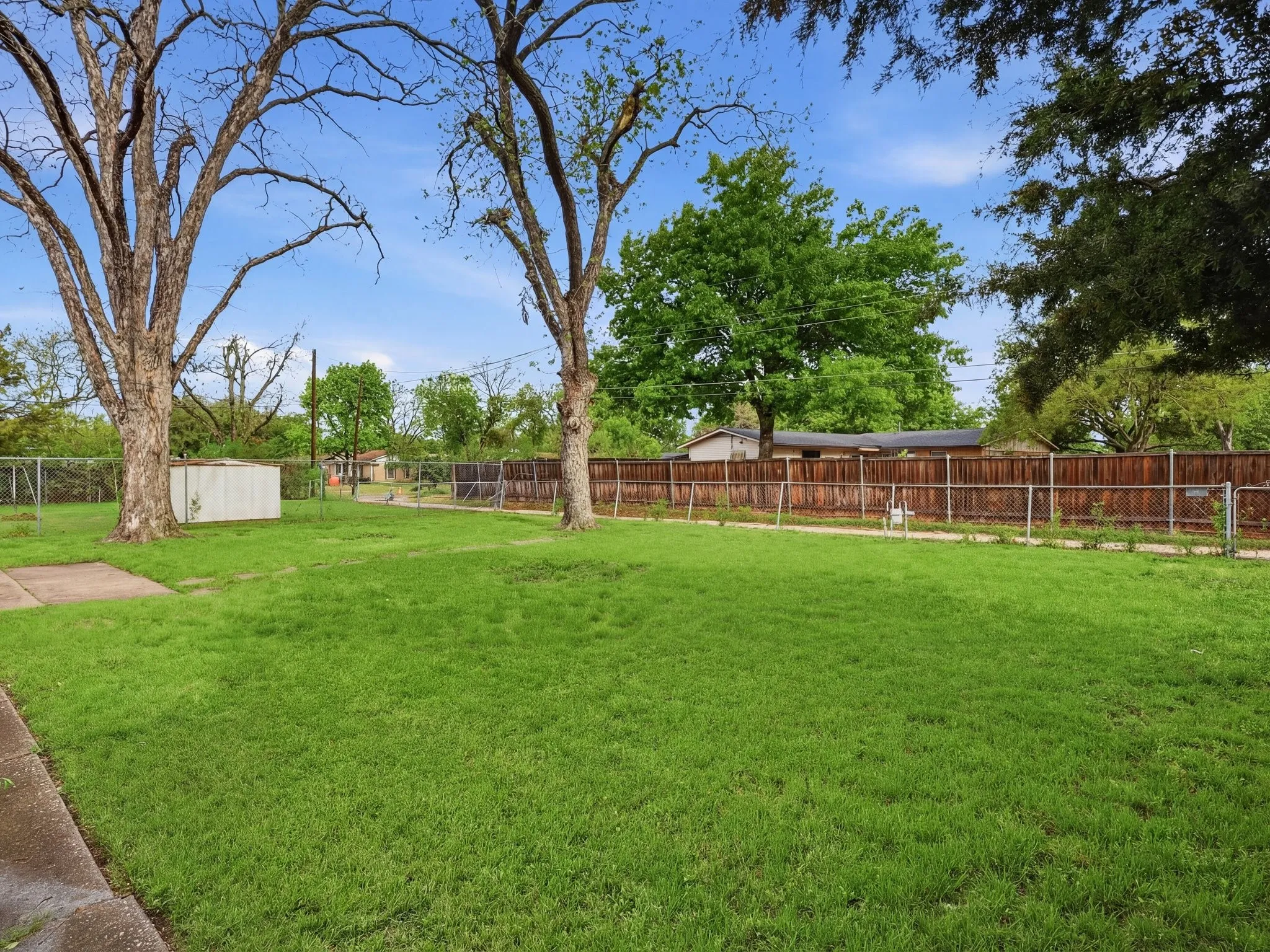 Expansive grass lawn with mature trees, chain-link fencing, and a wood privacy fence