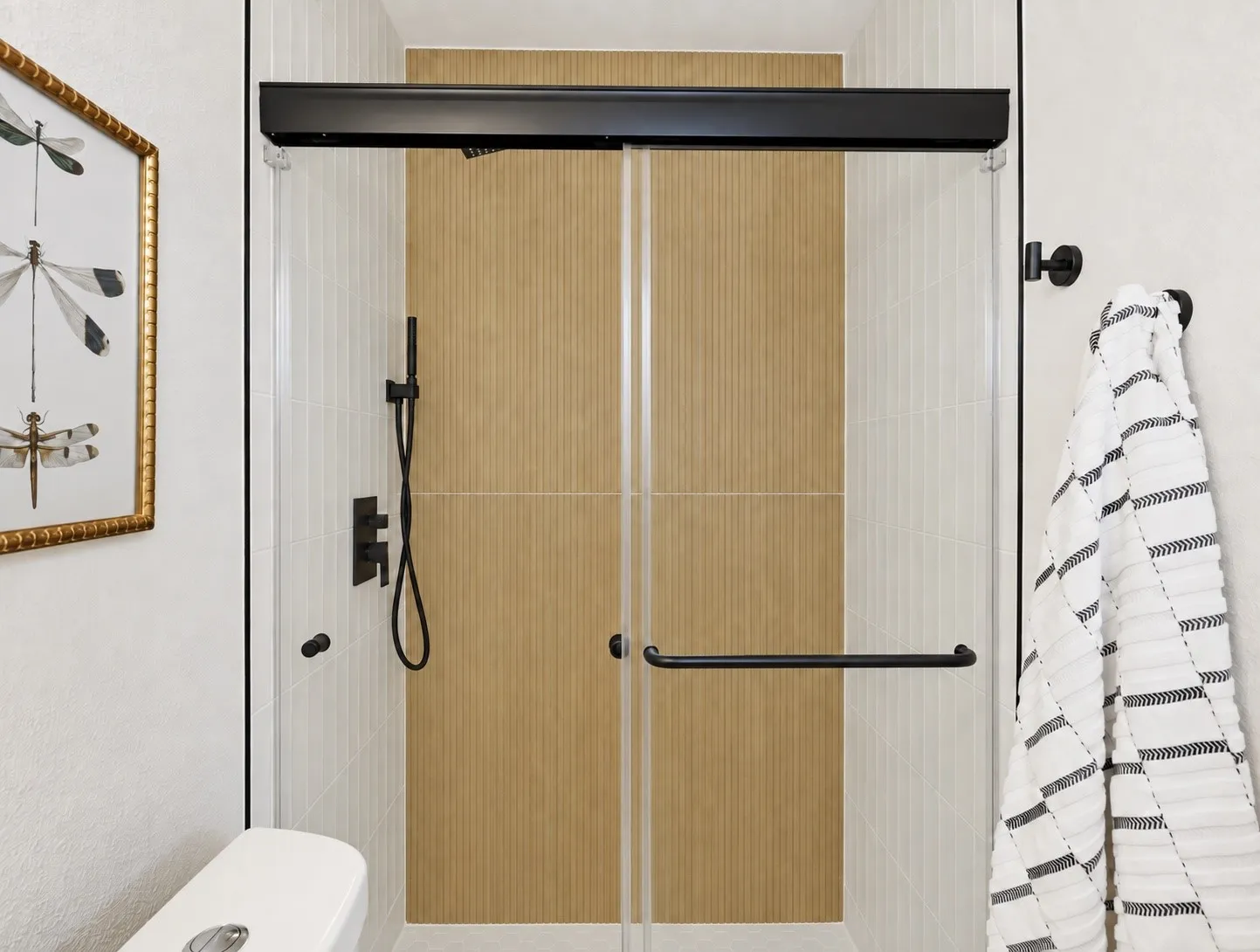 Glass-enclosed shower with matte black fixtures, full-height tile surround, and a coordinating shower floor