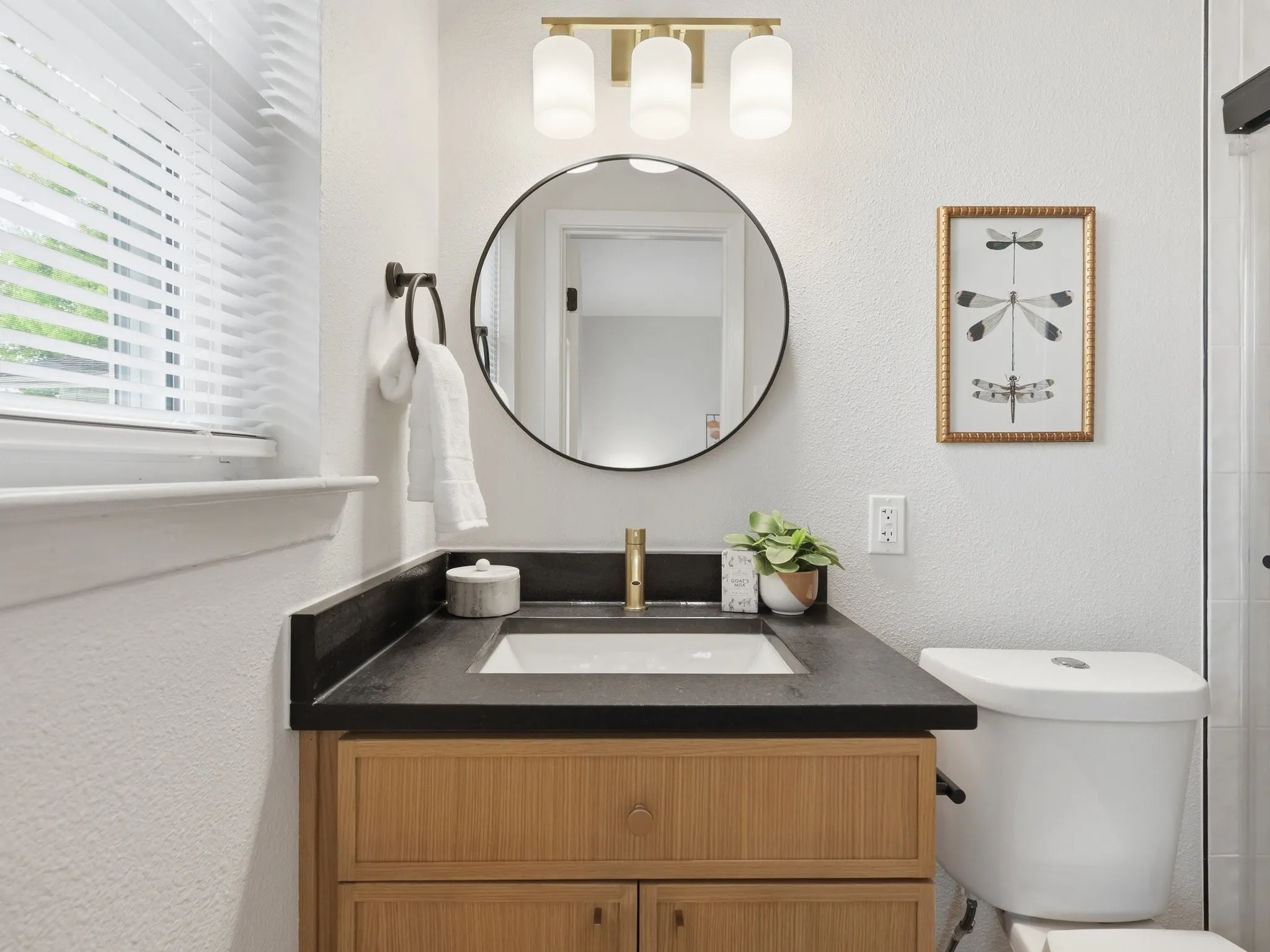 Wood-finish vanity with an integrated sink, dark countertop, and a round wall-mounted mirror