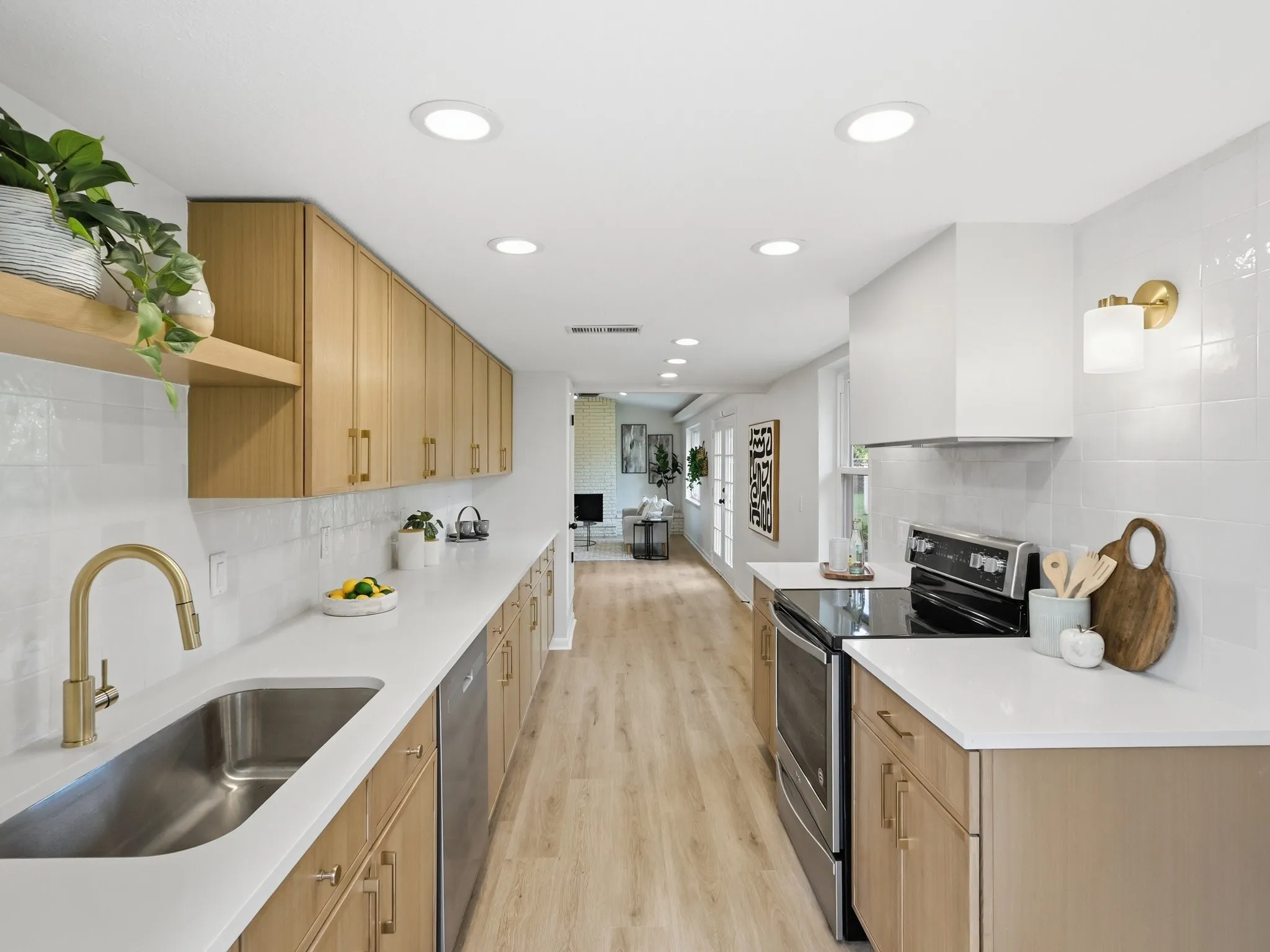 Galley kitchen featuring wood-finish cabinetry, stainless steel appliances, a stainless steel sink with a gold-tone faucet, and white countertops