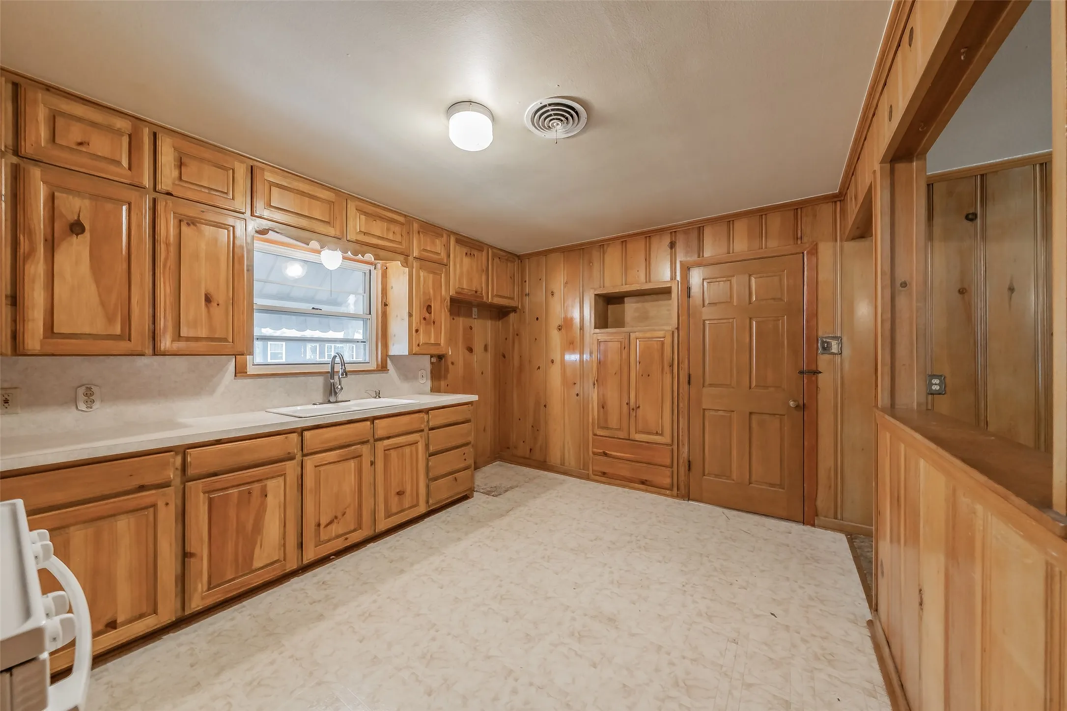 Kitchen featuring extensive wood cabinetry, white countertops, a stainless steel sink, and wall paneling