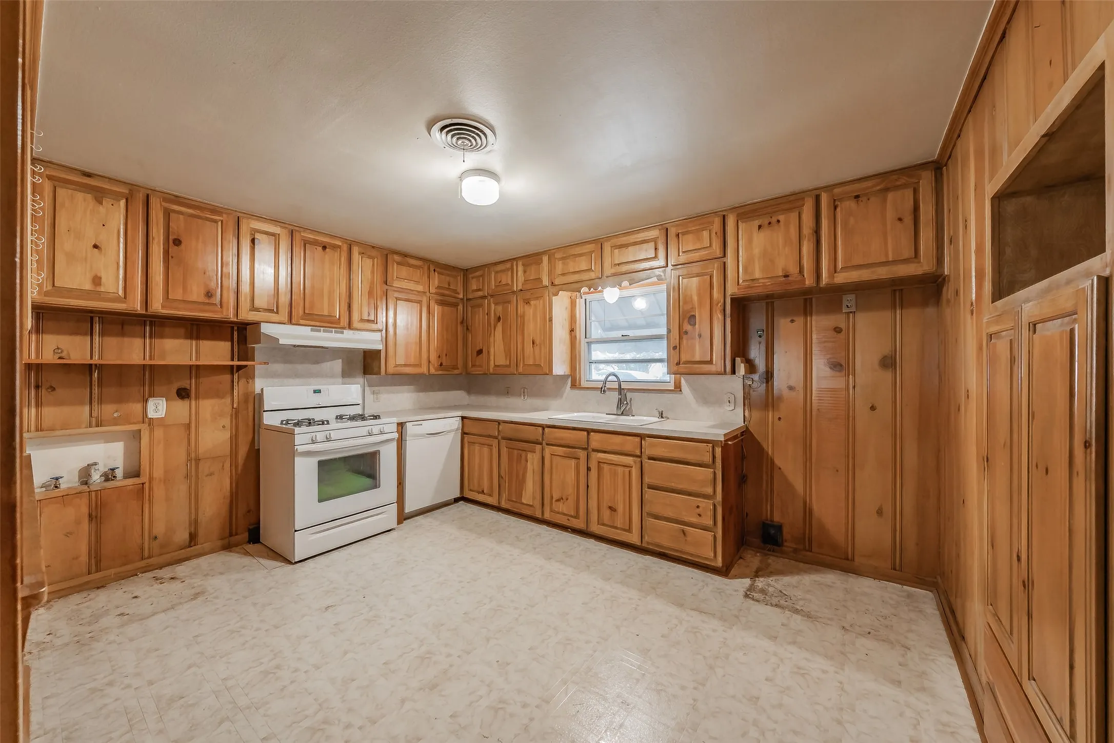 Kitchen featuring extensive wood cabinetry, white appliances, a stainless steel sink with a gooseneck faucet, and a window above the sink