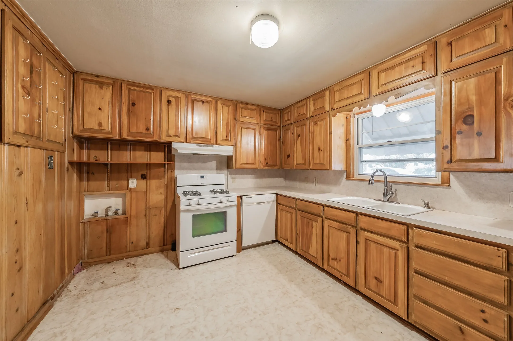 Wood-paneled kitchen featuring extensive cabinetry, white countertops, a double-basin sink with a gooseneck faucet, a white range with an oven, and a white dishwasher