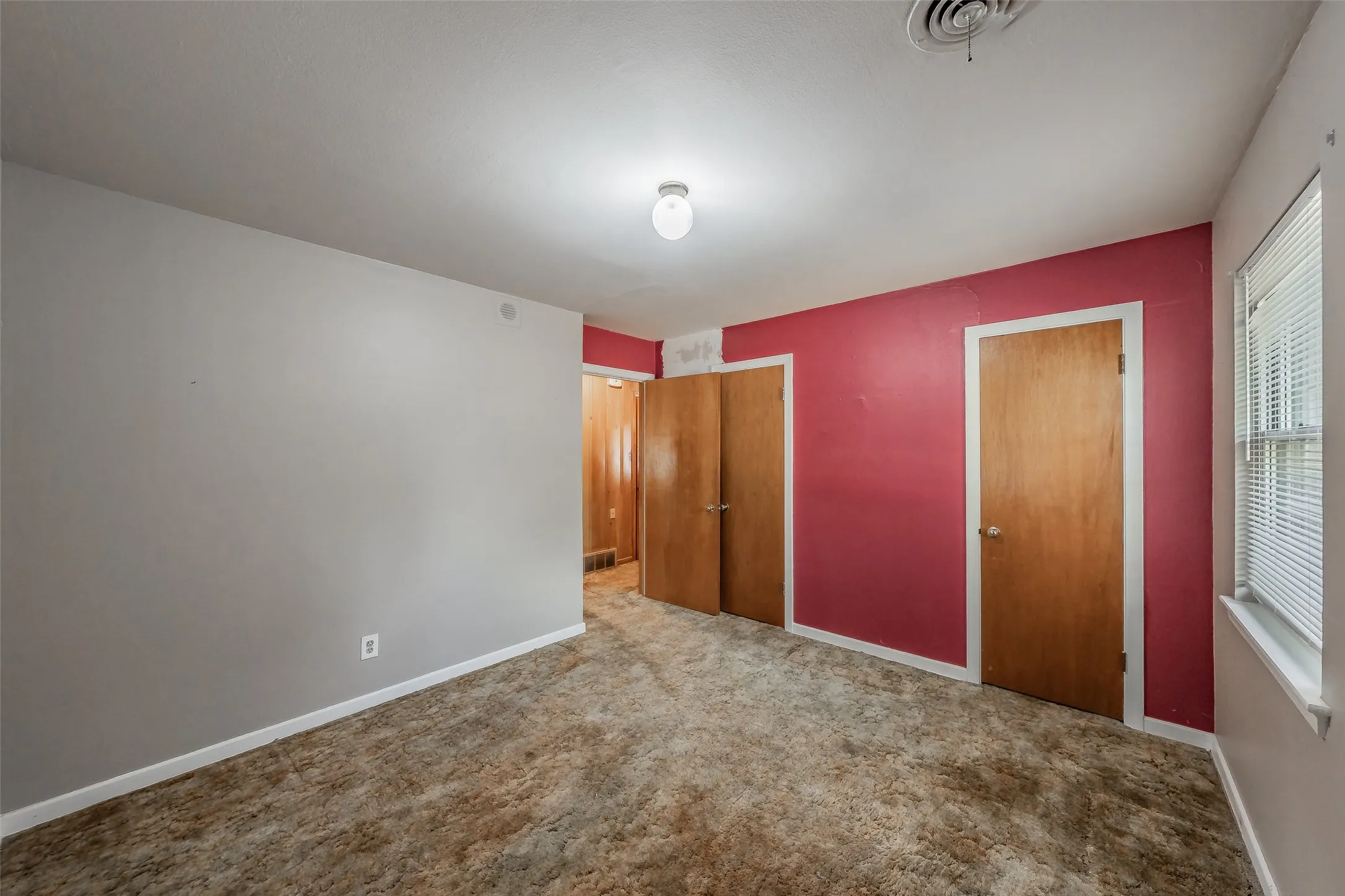 Wall-to-wall carpeting with multiple wood doors, a single window, and a ceiling-mounted light fixture