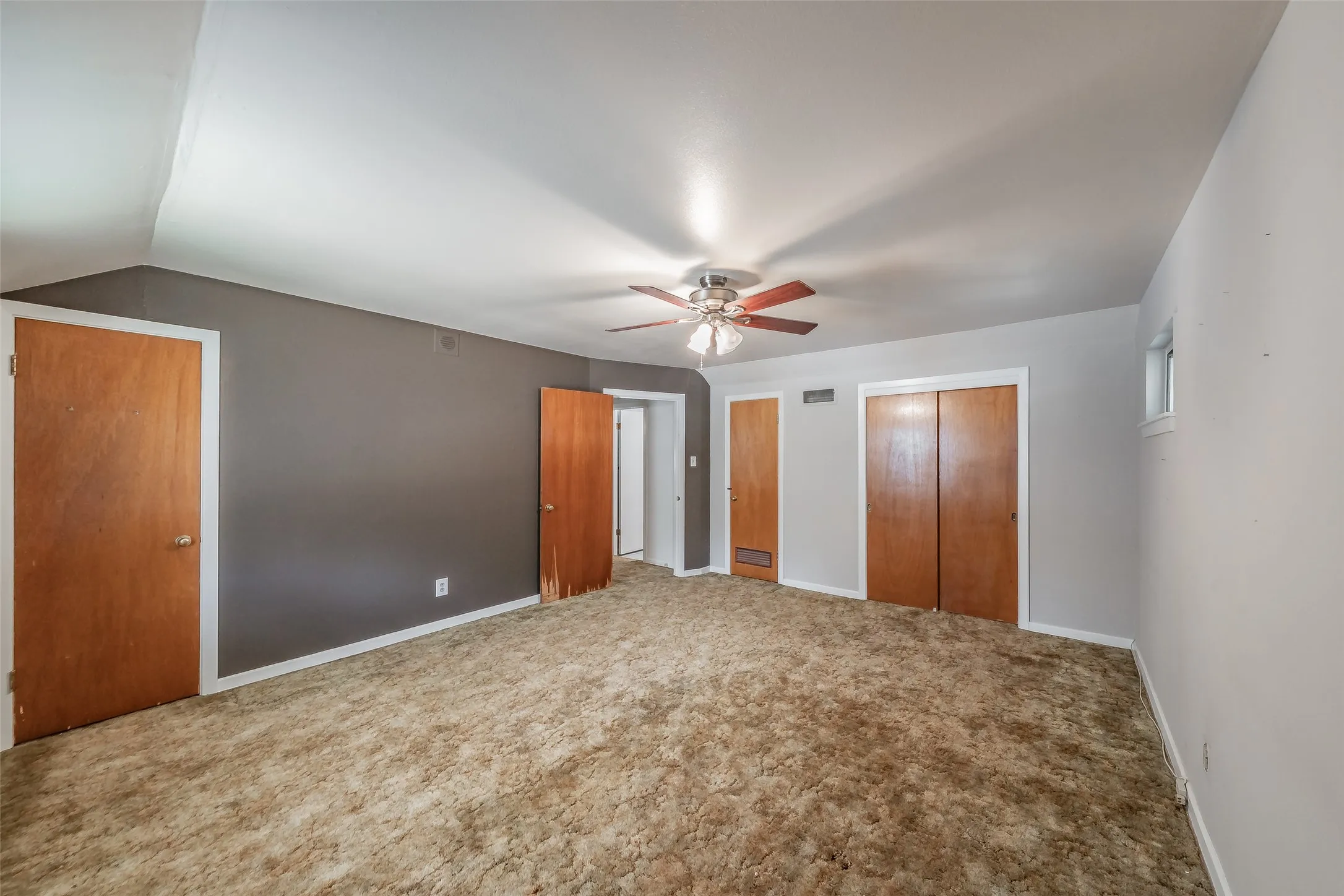 Spacious room featuring a ceiling fan, multiple wood-finish doors, and a window