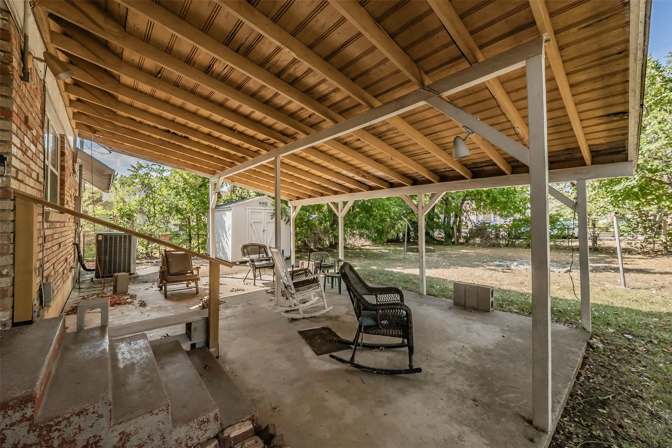 Covered patio with exposed wood ceiling, concrete flooring, and brick exterior
