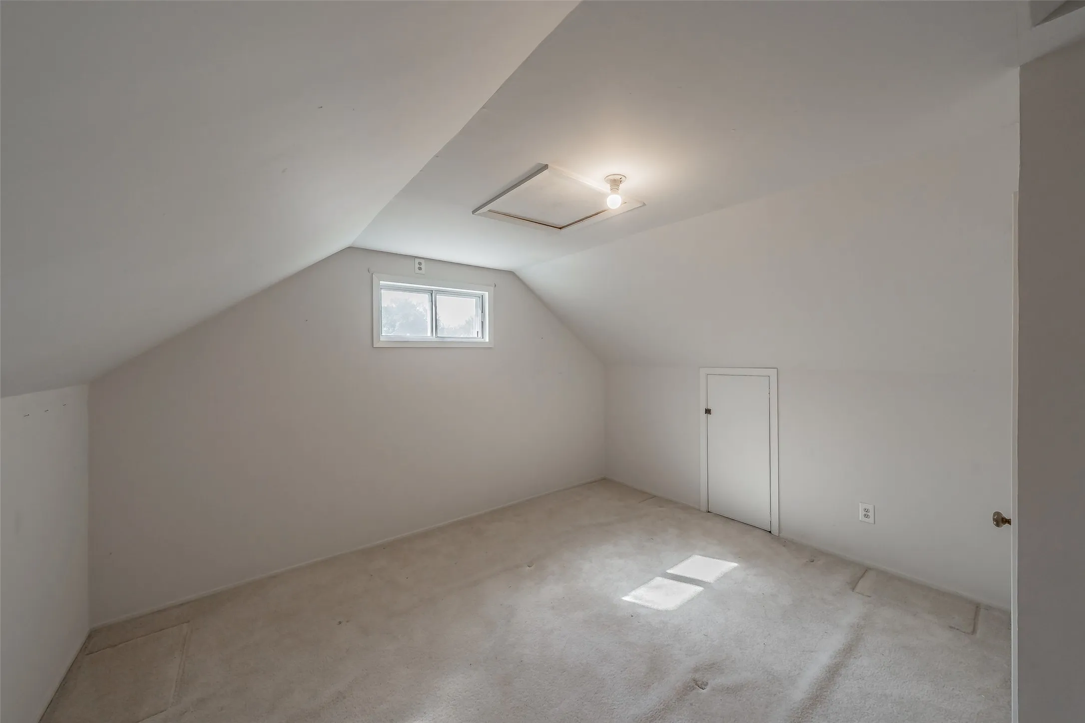 Carpeted room with sloped ceilings, a single window, and an access panel