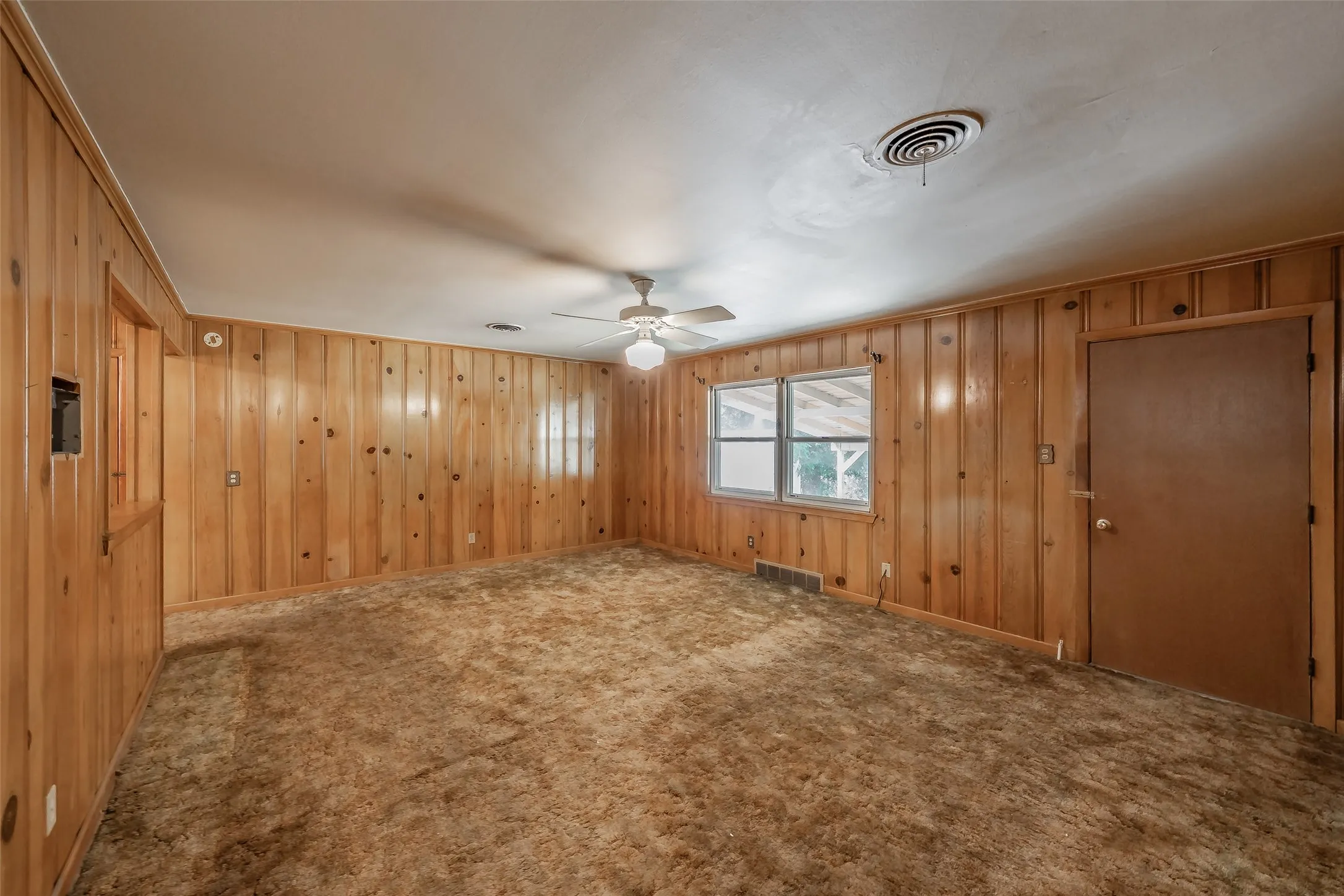 Wood paneling accents walls, white ceiling with ceiling fan, and carpeted flooring