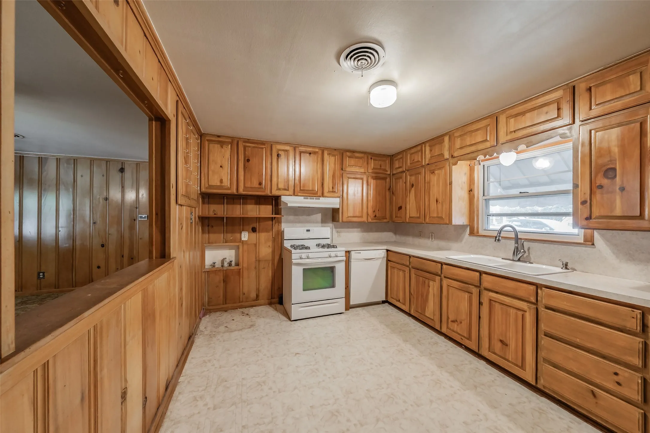 Spacious kitchen featuring rich wood cabinetry throughout, white appliances, light-toned countertops, and a large window overlooking the exterior