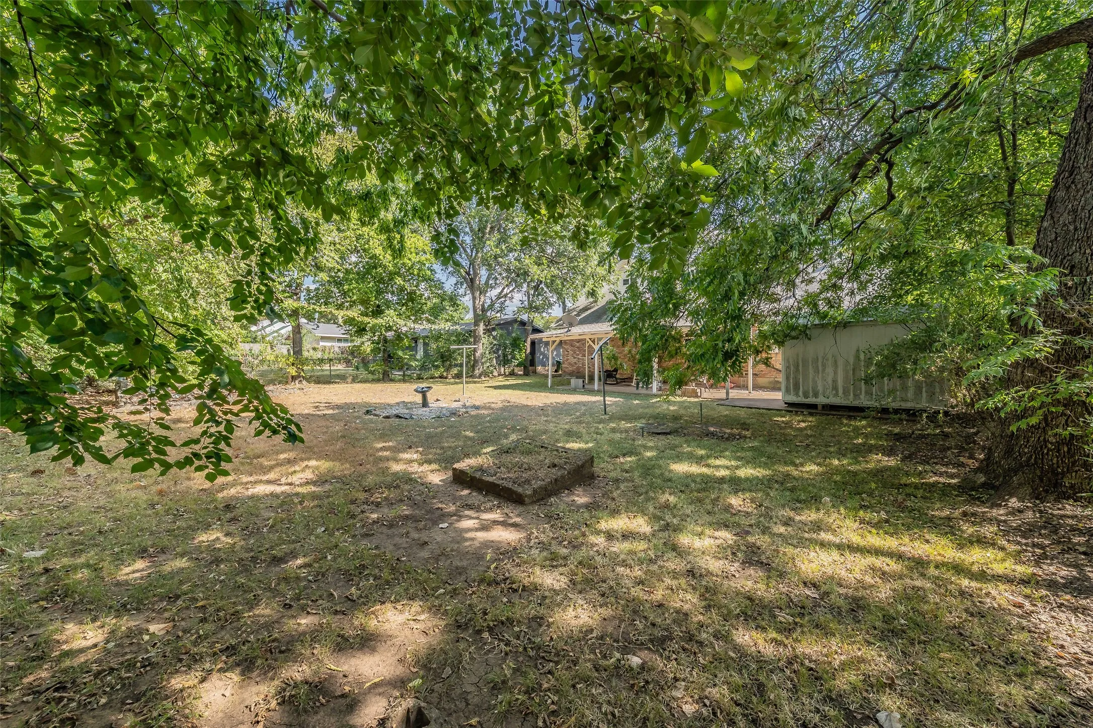 Expansive rear yard featuring mature trees, a covered patio, and a storage structure