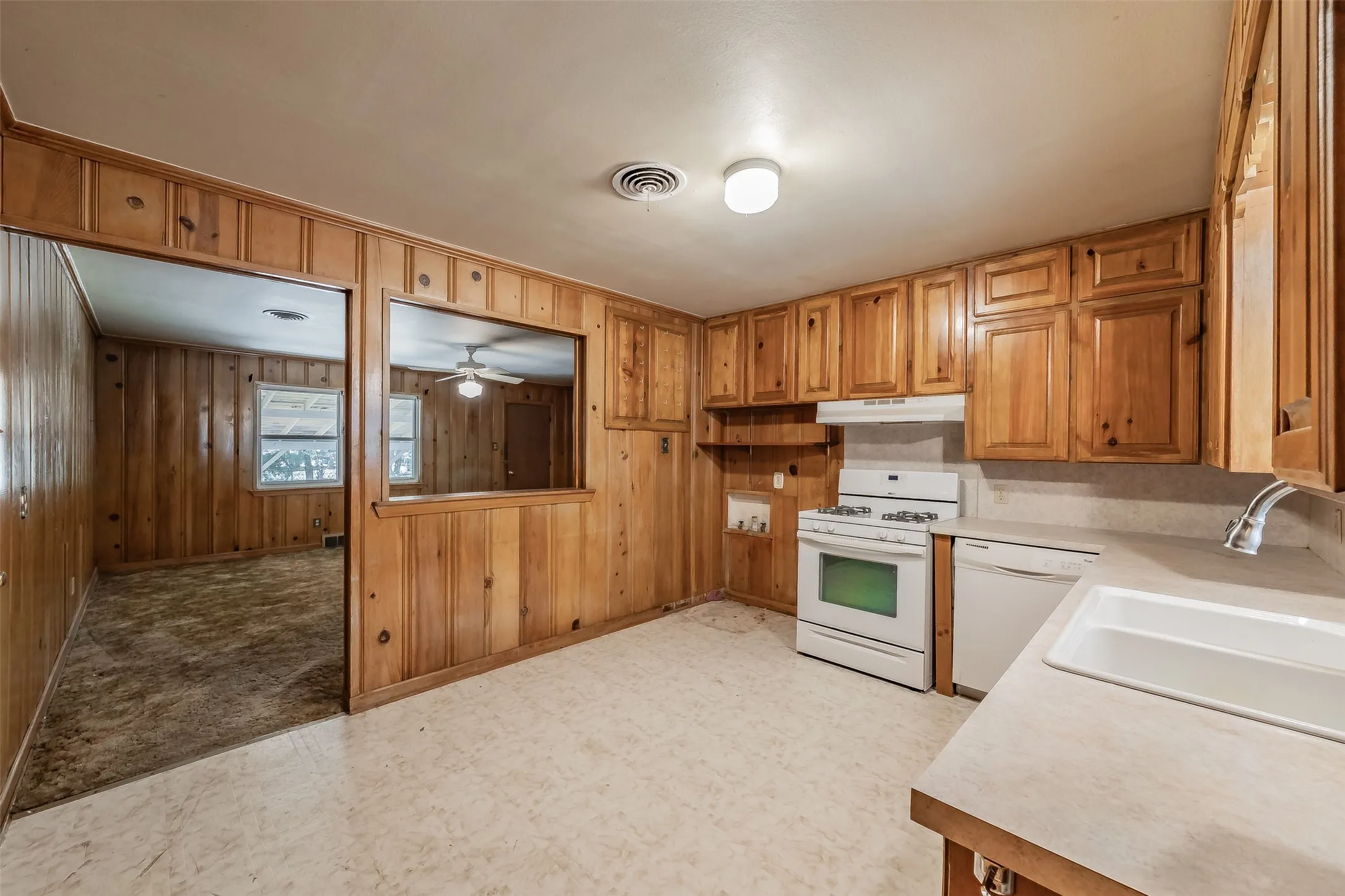 Kitchen featuring wood cabinetry, white gas range, white dishwasher, and a pass-through opening to an adjacent room