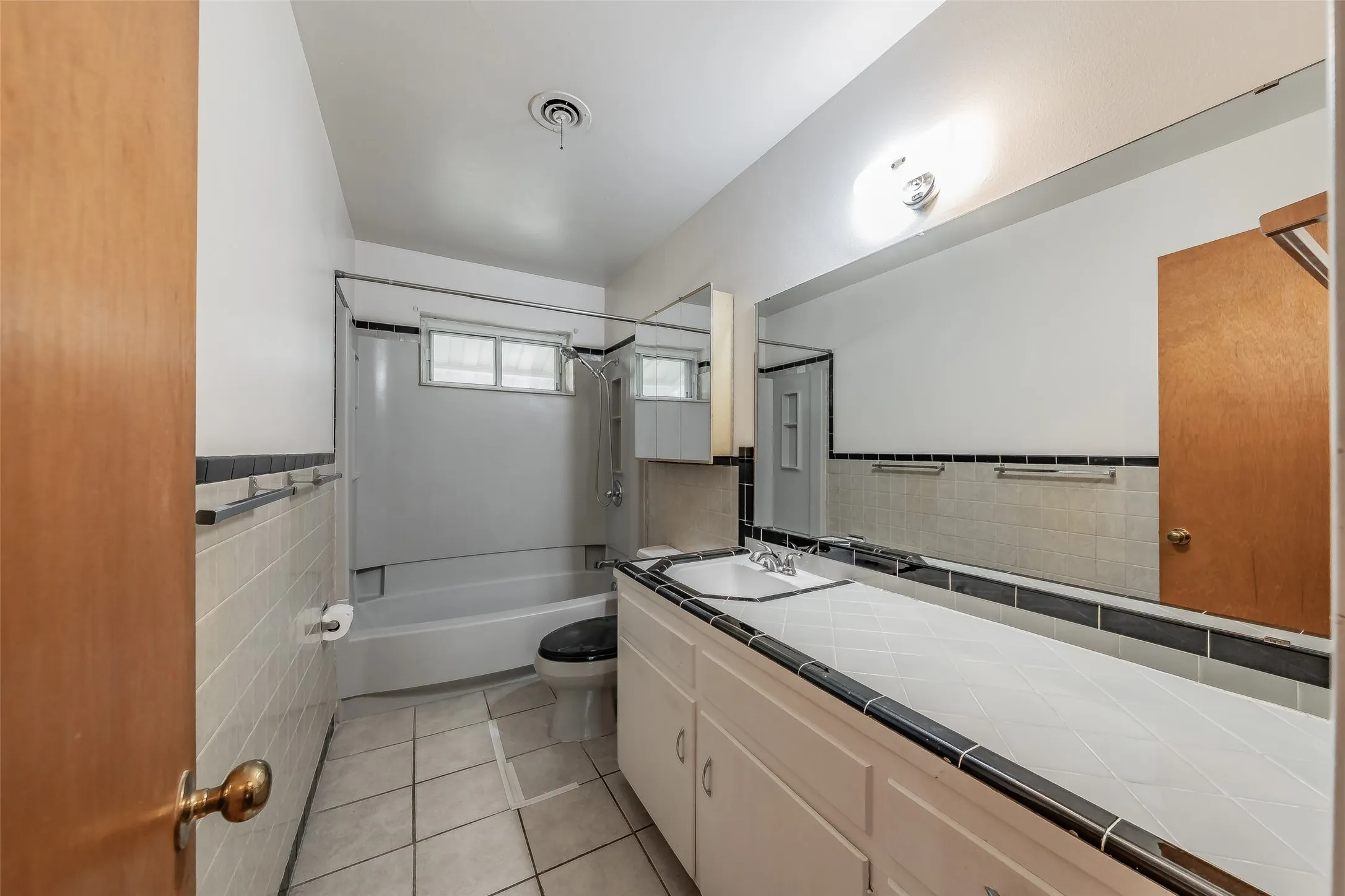 White tile flooring with dark grout, full vanity with integrated sink, expansive wall mirror, built-in medicine cabinet, and a shower-tub combination