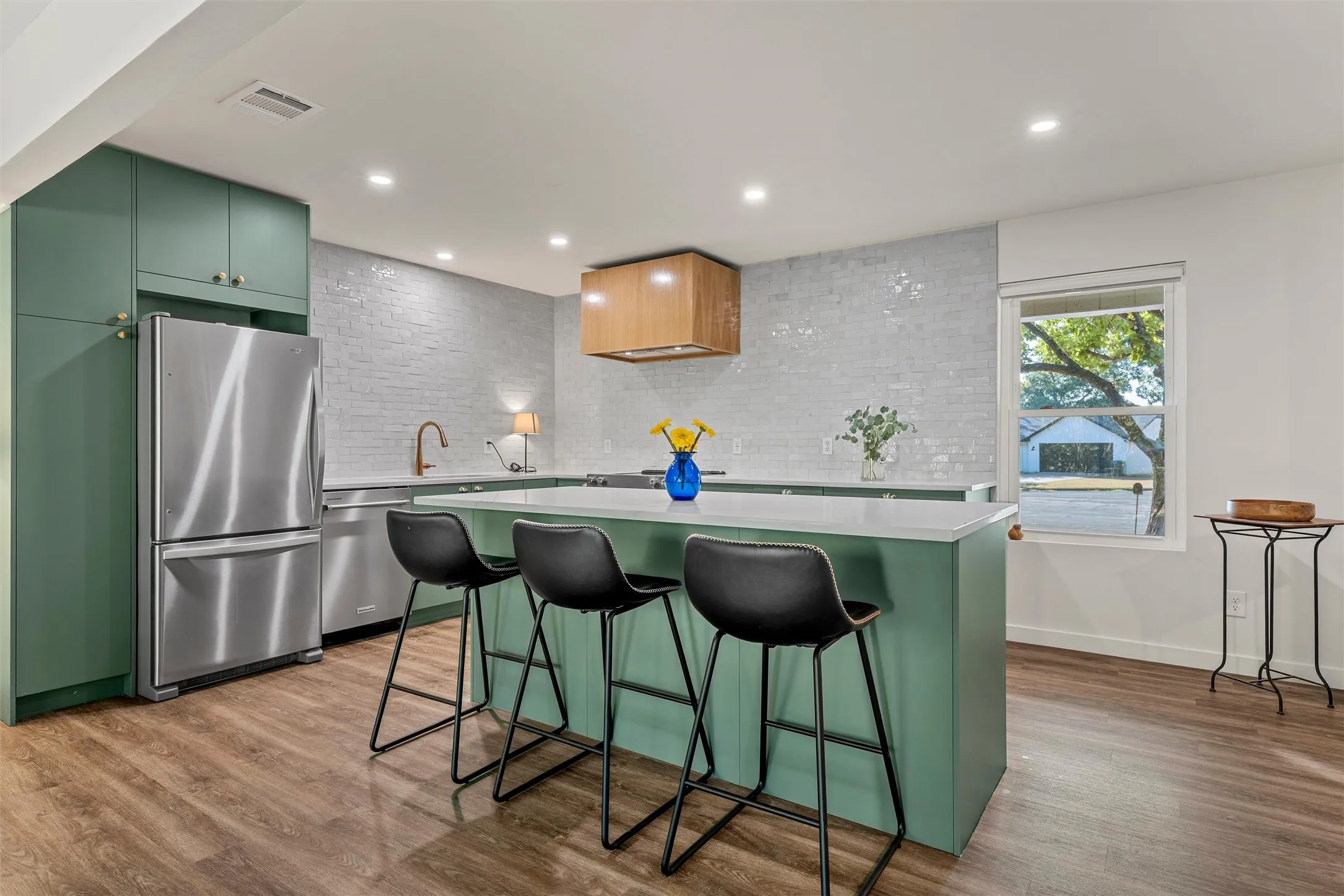 Kitchen featuring wood-finish flooring, recessed lighting, green cabinetry, a white countertop island, and stainless steel appliances