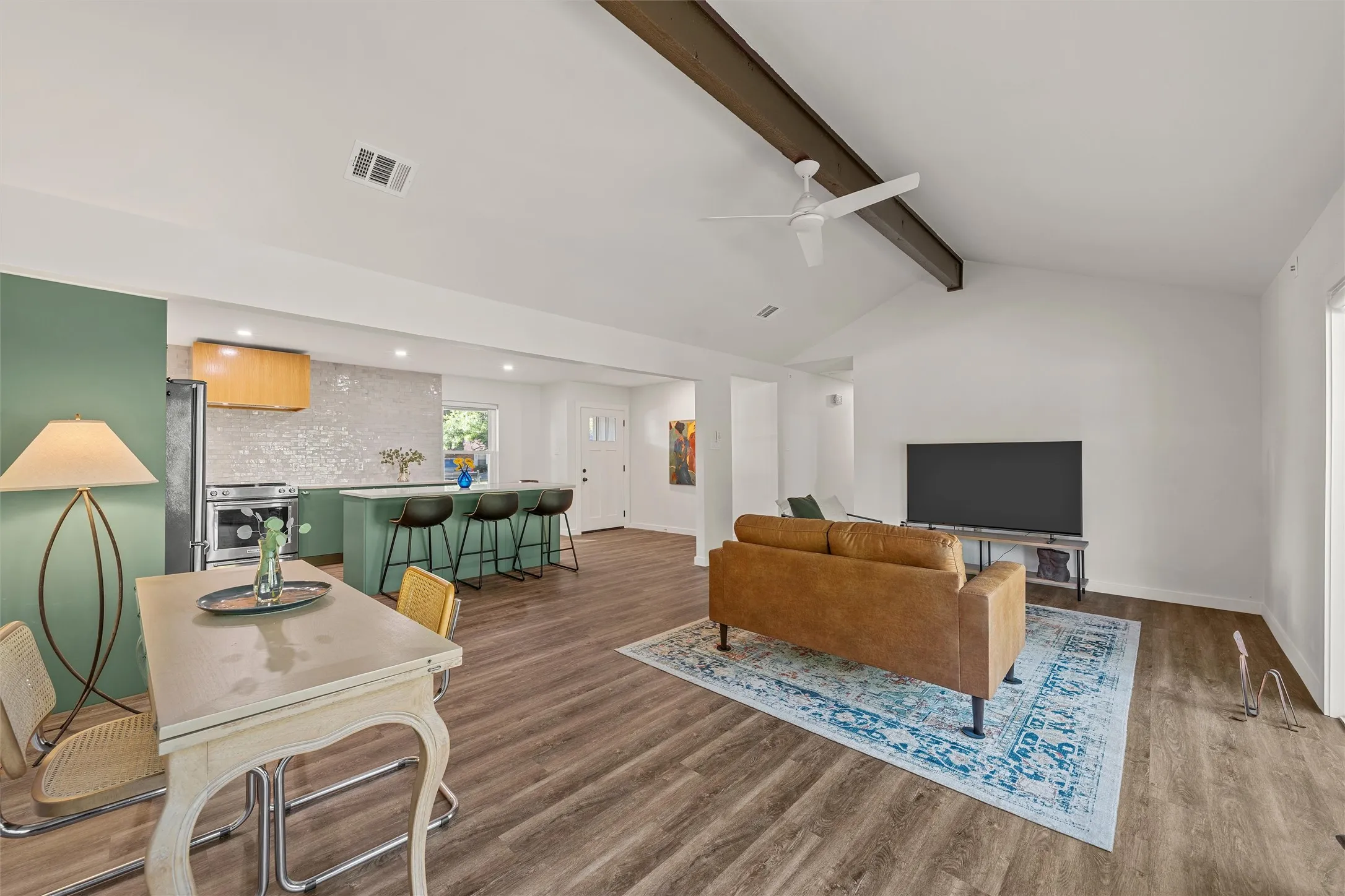 Vaulted ceiling with exposed wood beam, wood-finish flooring, recessed lighting, kitchen island with seating, and a mosaic tile backsplash
