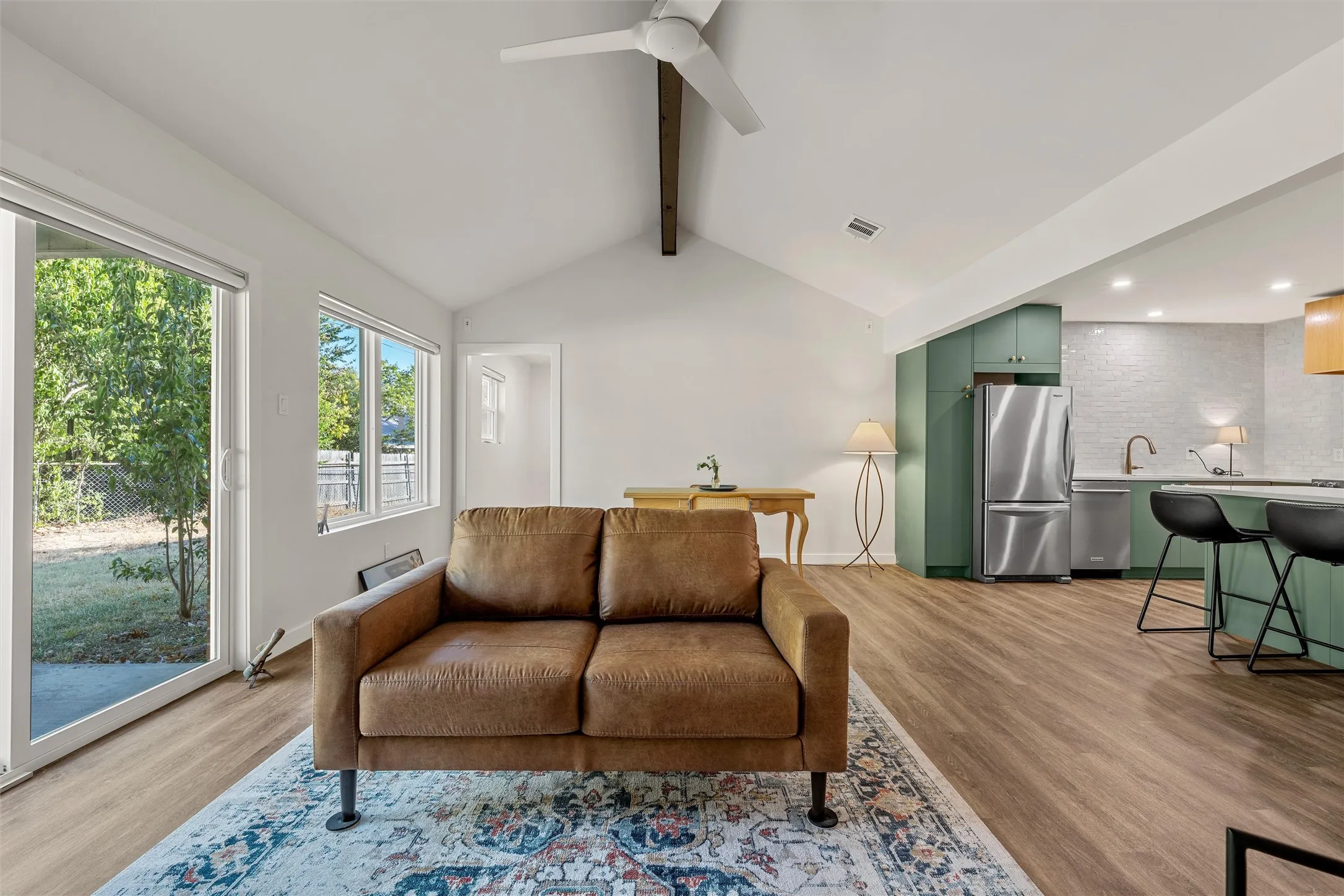 Vaulted ceiling with exposed beam, wood-finish flooring, sliding glass door, modern ceiling fan, and updated kitchen with stainless steel appliances