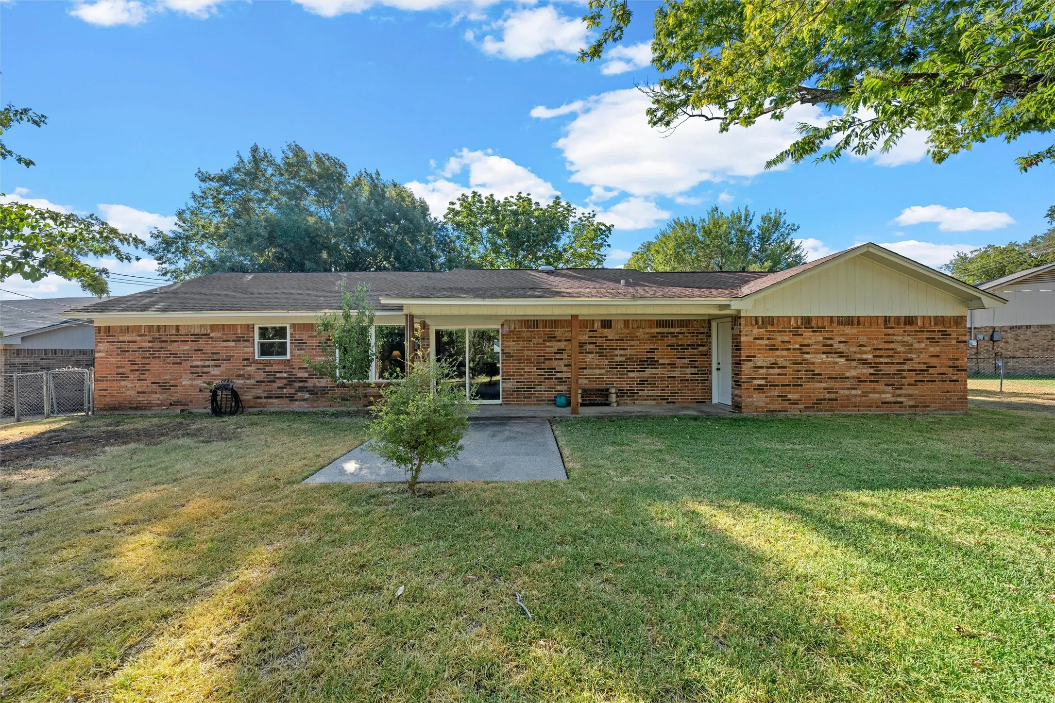Brick exterior with a covered patio, expansive lawn, and sliding glass door