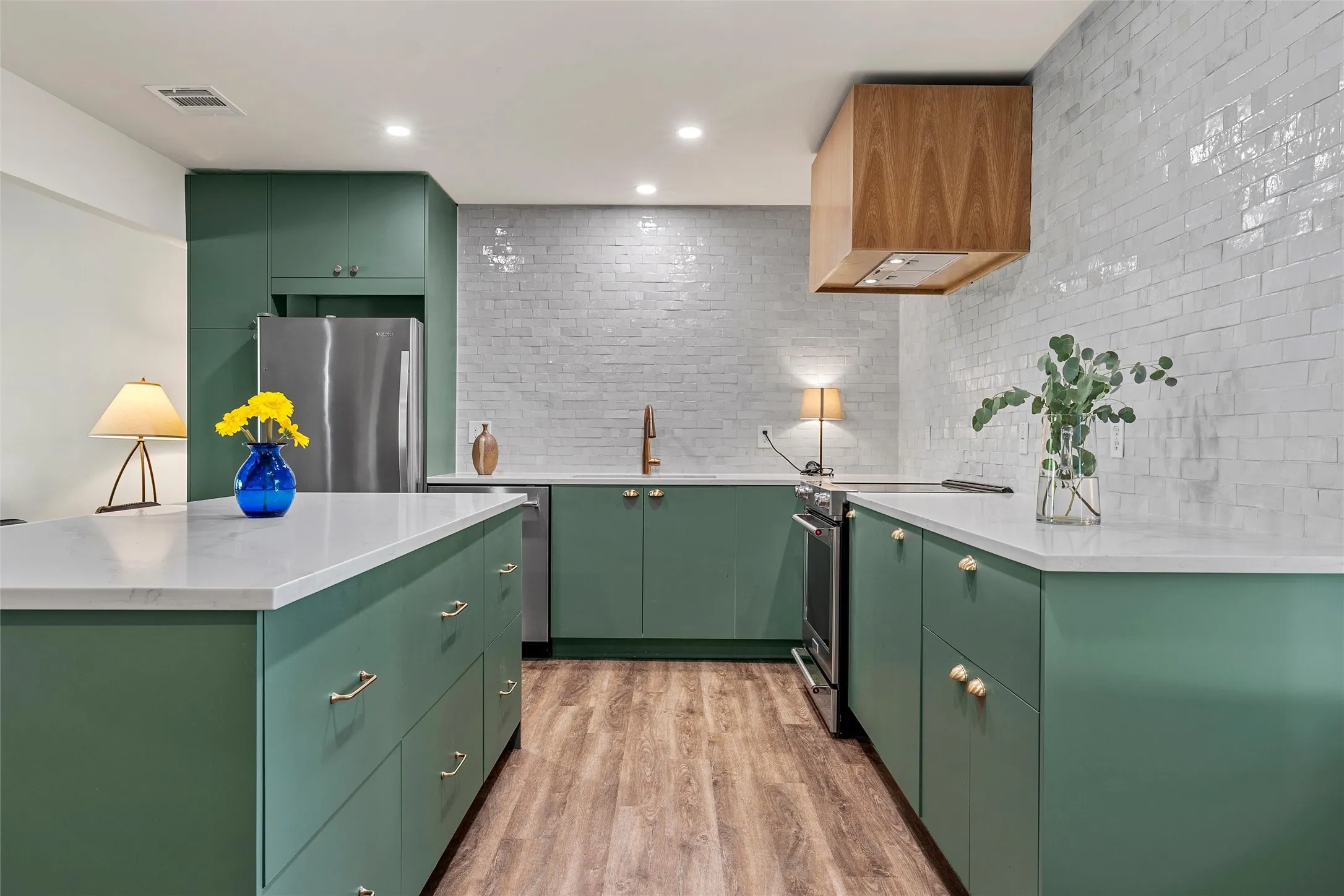 Kitchen featuring green cabinetry, light-toned countertops, a light-toned backsplash, wood-finish flooring, and a stainless steel appliance suite