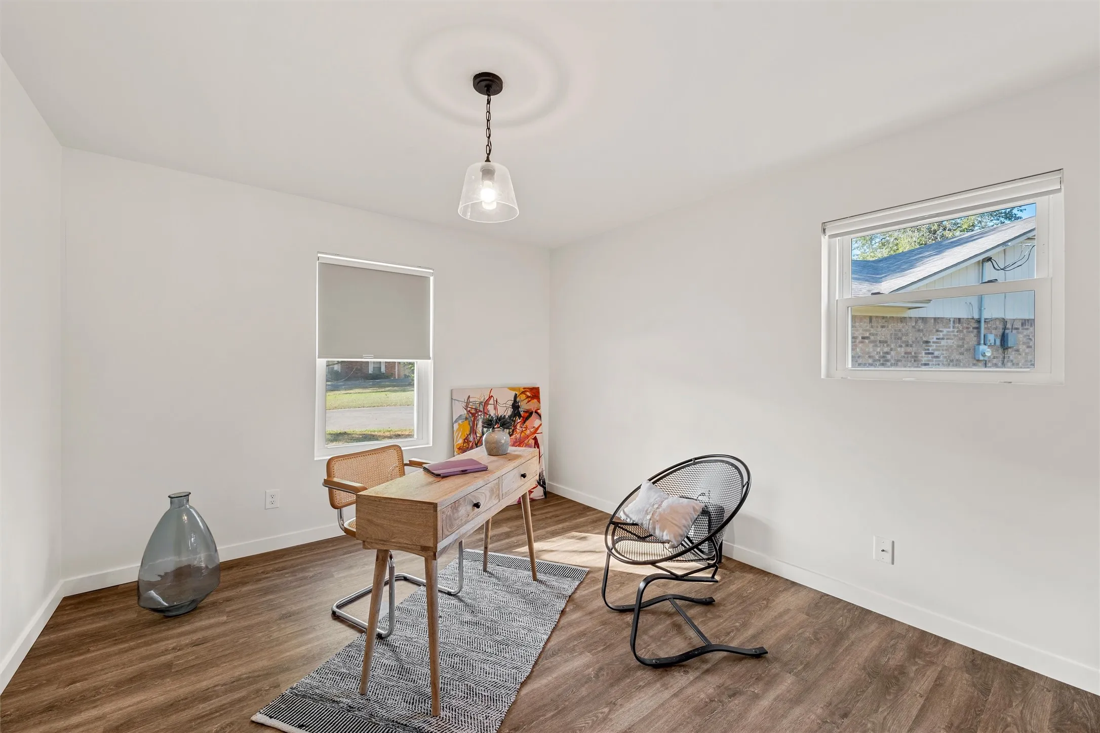 Wood-finish flooring, white walls, two windows with roller shades, and a ceiling-mounted pendant light fixture