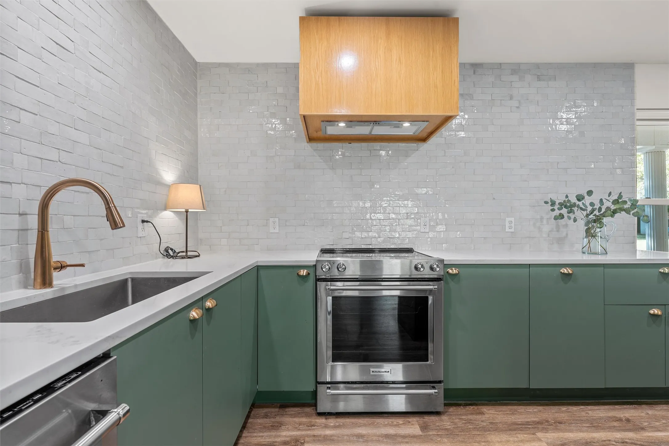 Kitchen featuring green cabinetry, light-colored countertops, stainless steel appliances, and a wood-finish range hood