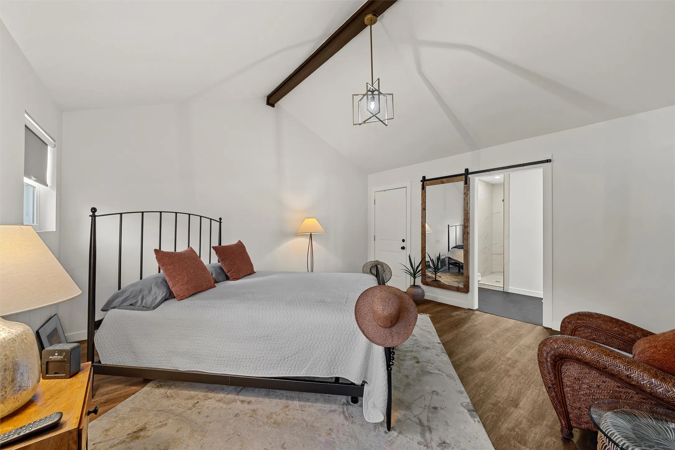 Vaulted ceiling with exposed wood beam, wood-finish flooring, white walls, and a barn door leading to an adjacent space