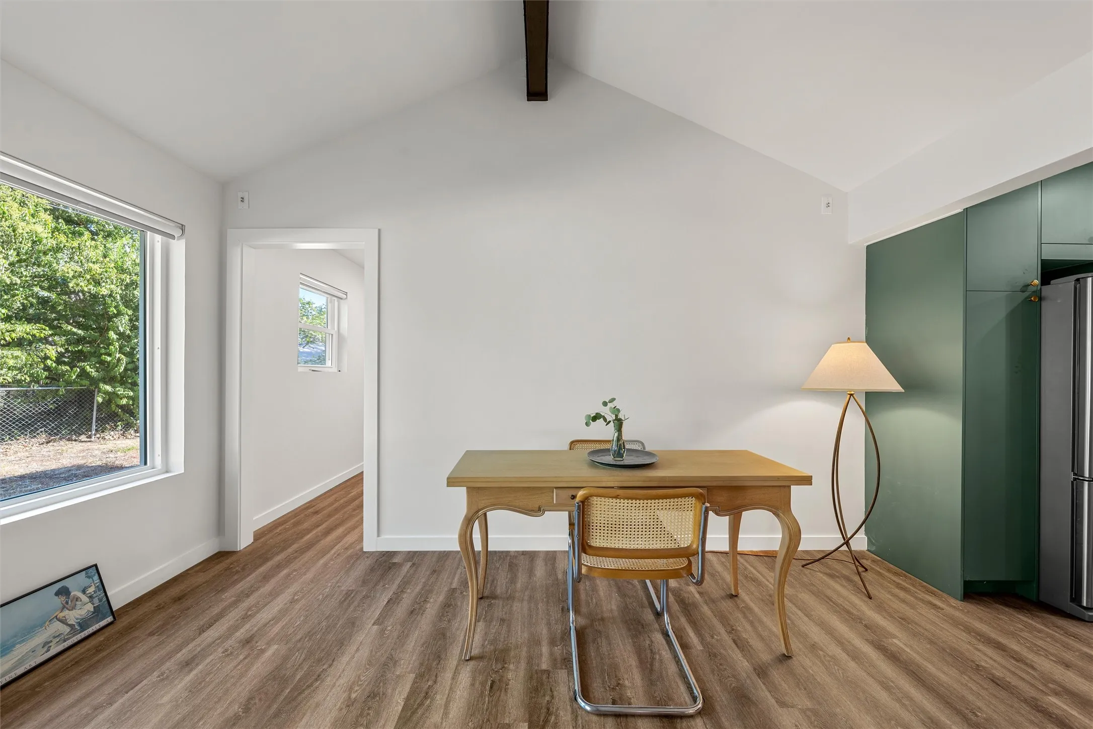 Vaulted ceiling, wood-finish flooring, white walls, large window, and built-in green cabinetry