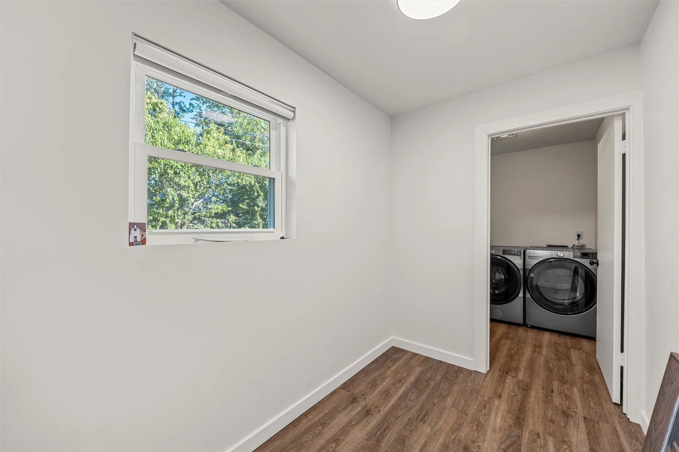 Wood-finish flooring, white walls, and a window with a roller shade