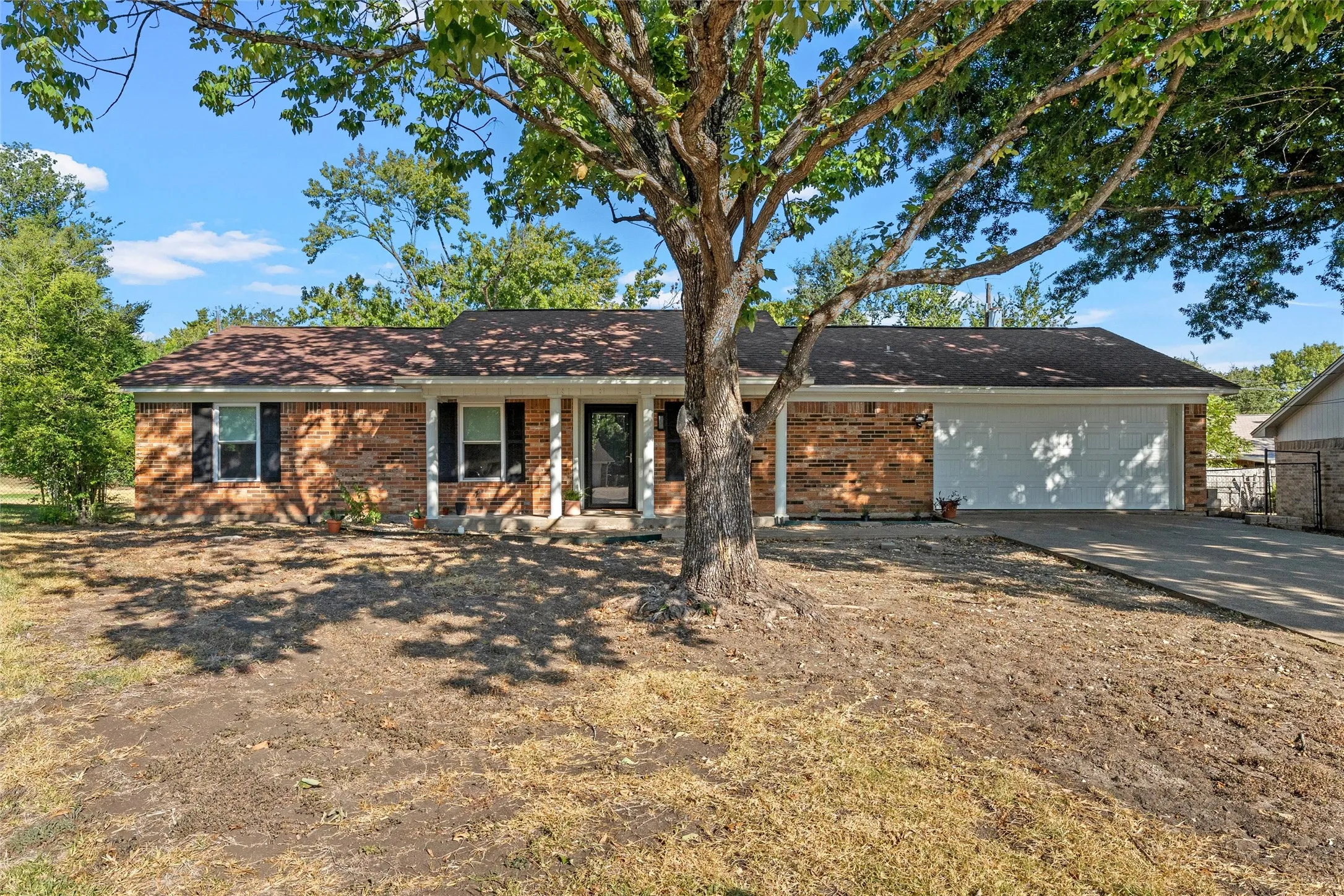 Brick facade, covered front entry, two-car garage, mature front yard tree, concrete driveway