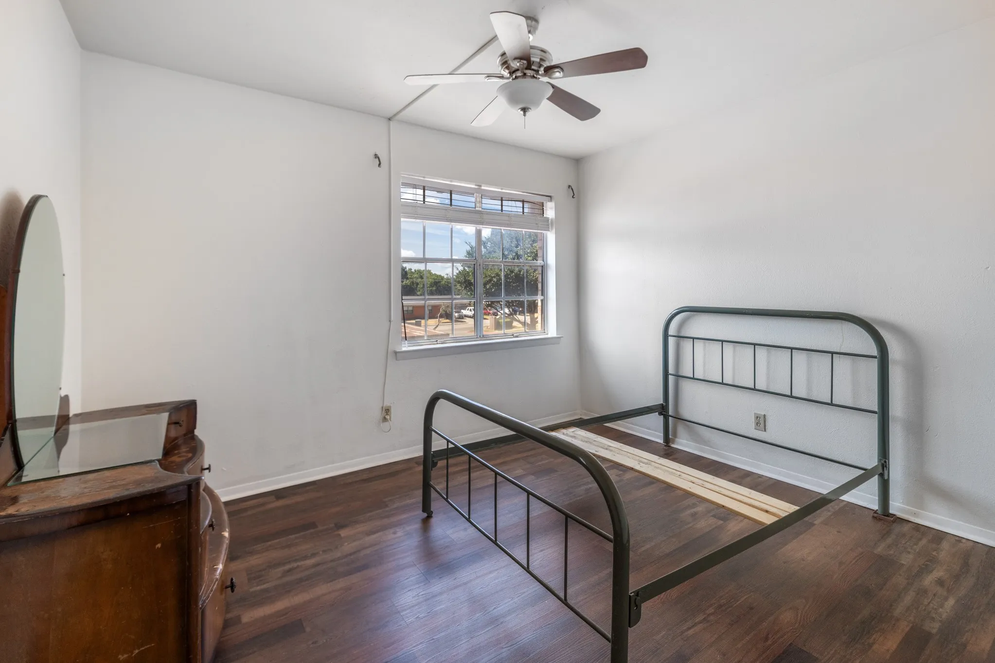 Wood-finish flooring, ceiling fan with light fixture, and window with exterior landscaping