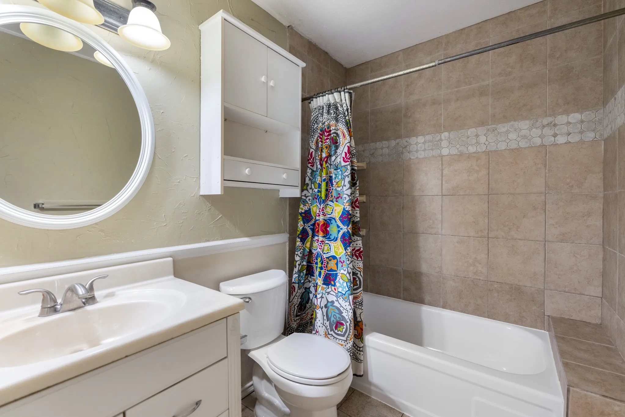 Bathroom featuring a vanity with an integrated sink, a circular wall mirror, and a wall-mounted storage cabinet