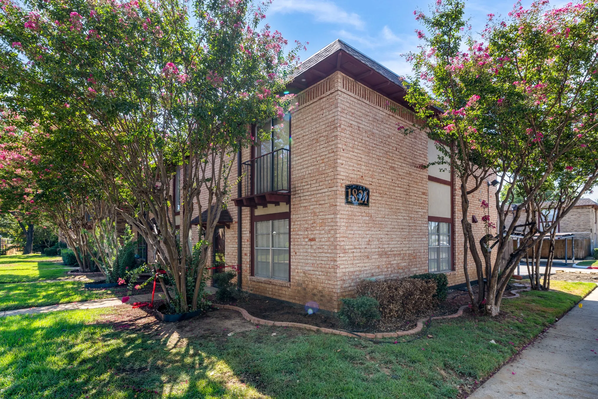 Brick exterior with contrasting trim, second-story balcony with iron railing, and established landscaping with flowering trees