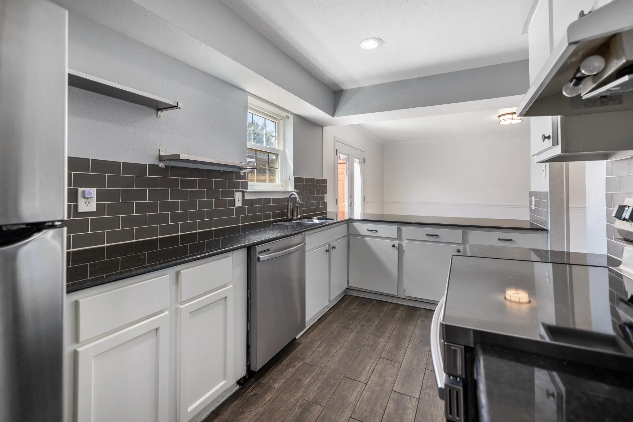 Kitchen featuring wood-finish flooring, white cabinetry, dark countertops, dark subway tile backsplash, and stainless steel appliances