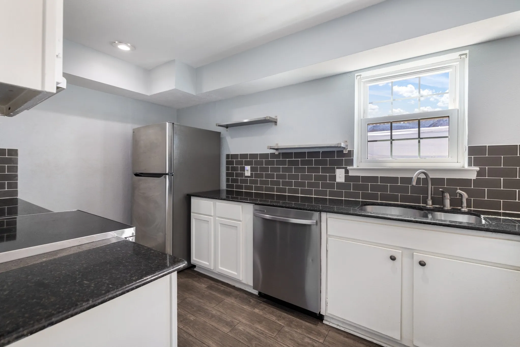 Kitchen featuring white cabinetry, dark stone countertops, dark subway tile backsplash, stainless steel appliances, and wood-finish flooring