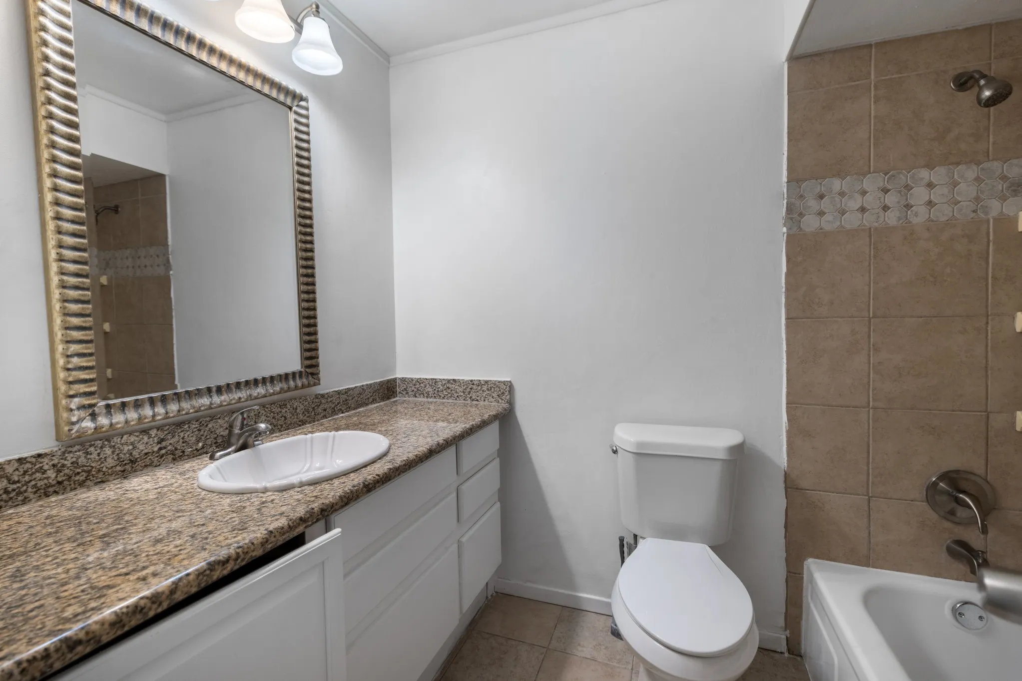 Bathroom featuring a vanity with an integrated sink, a large framed mirror, and a tiled shower with a decorative accent band