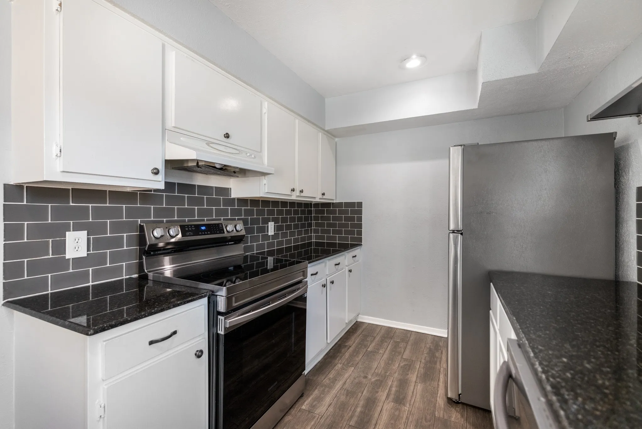White cabinetry, dark subway tile backsplash, black countertops, stainless steel appliances, and wood-finish flooring