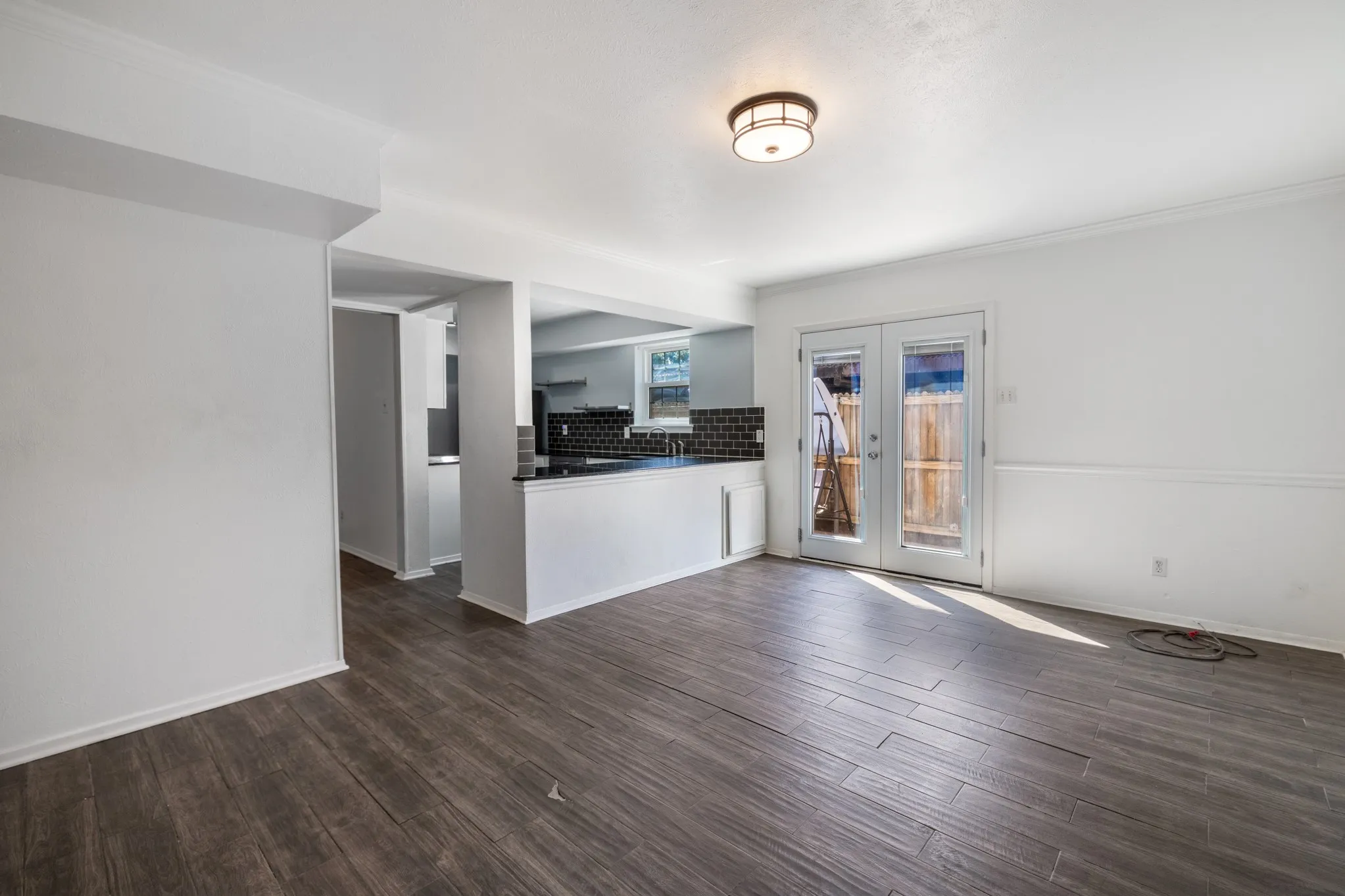 Wood-finish plank flooring, recessed wall opening, black subway tile backsplash, black countertop, and double glass-paned doors