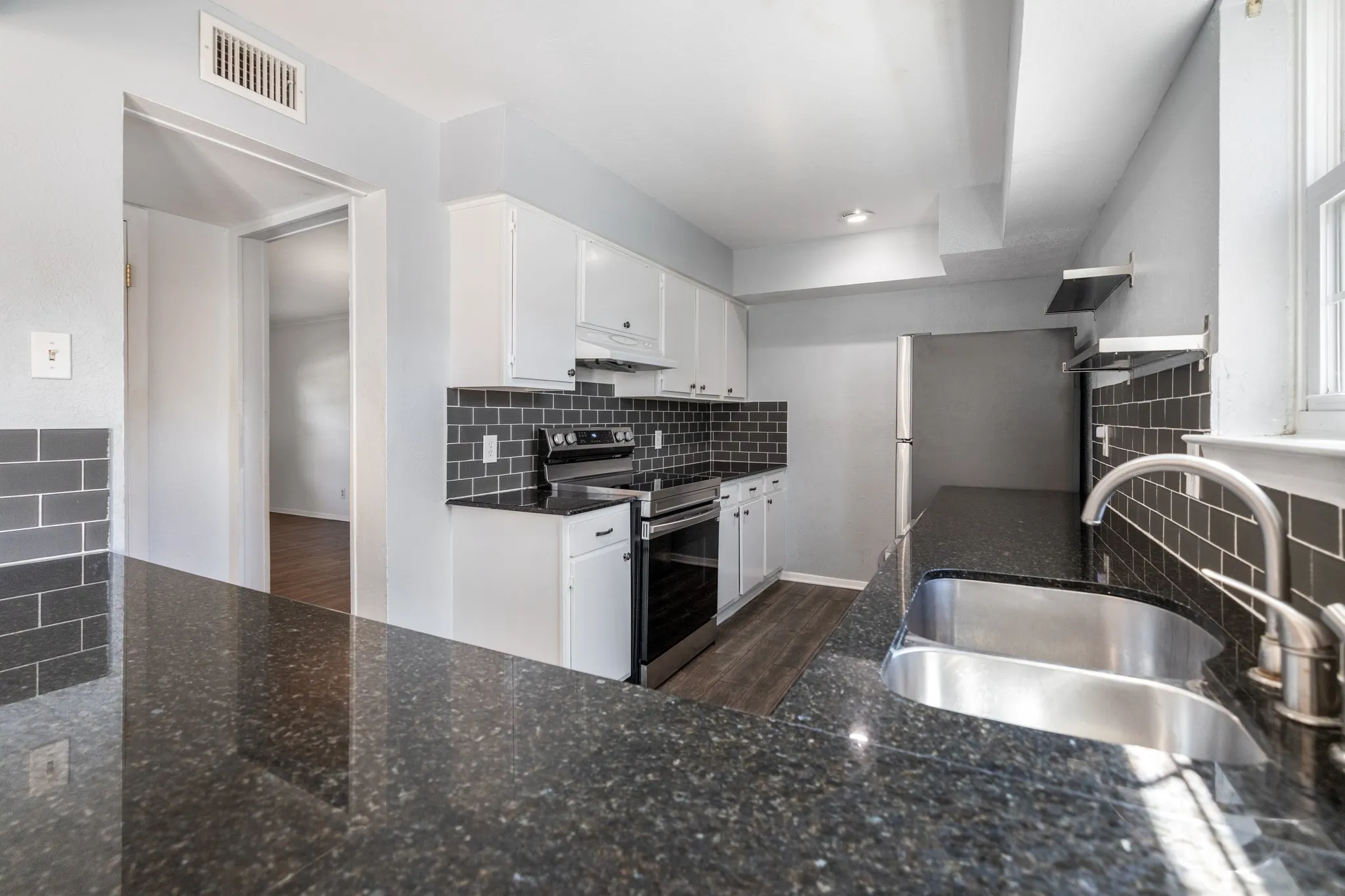 Kitchen featuring white upper and lower cabinetry, dark subway tile backsplash, dark speckled countertops, and a double basin stainless steel sink with a gooseneck faucet