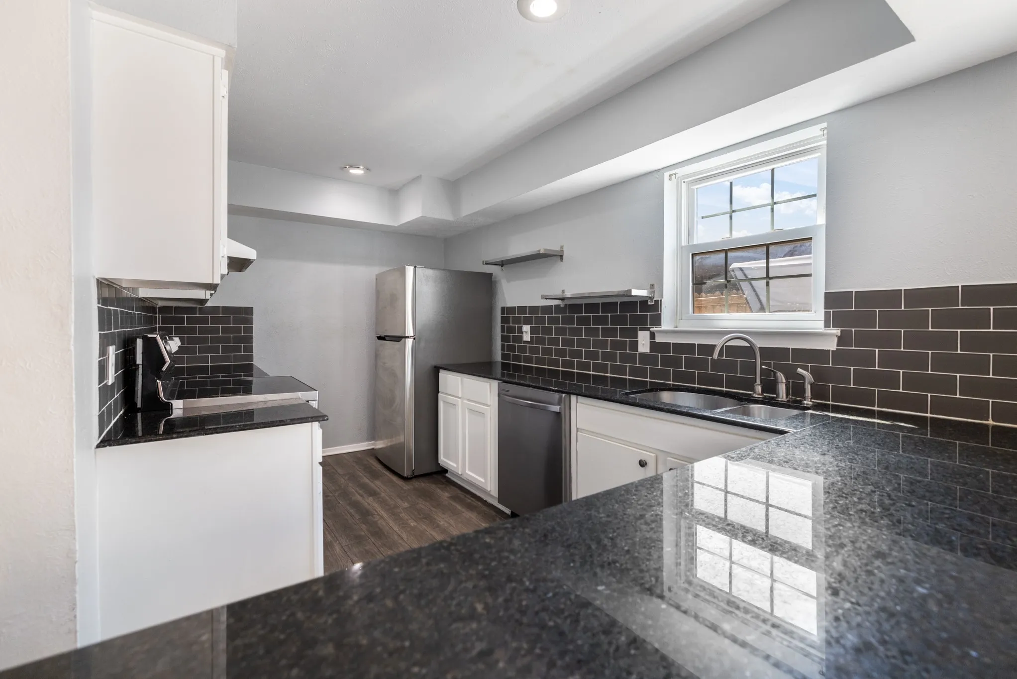 Kitchen featuring white cabinetry, dark subway tile backsplash, dark countertops, and stainless steel appliances