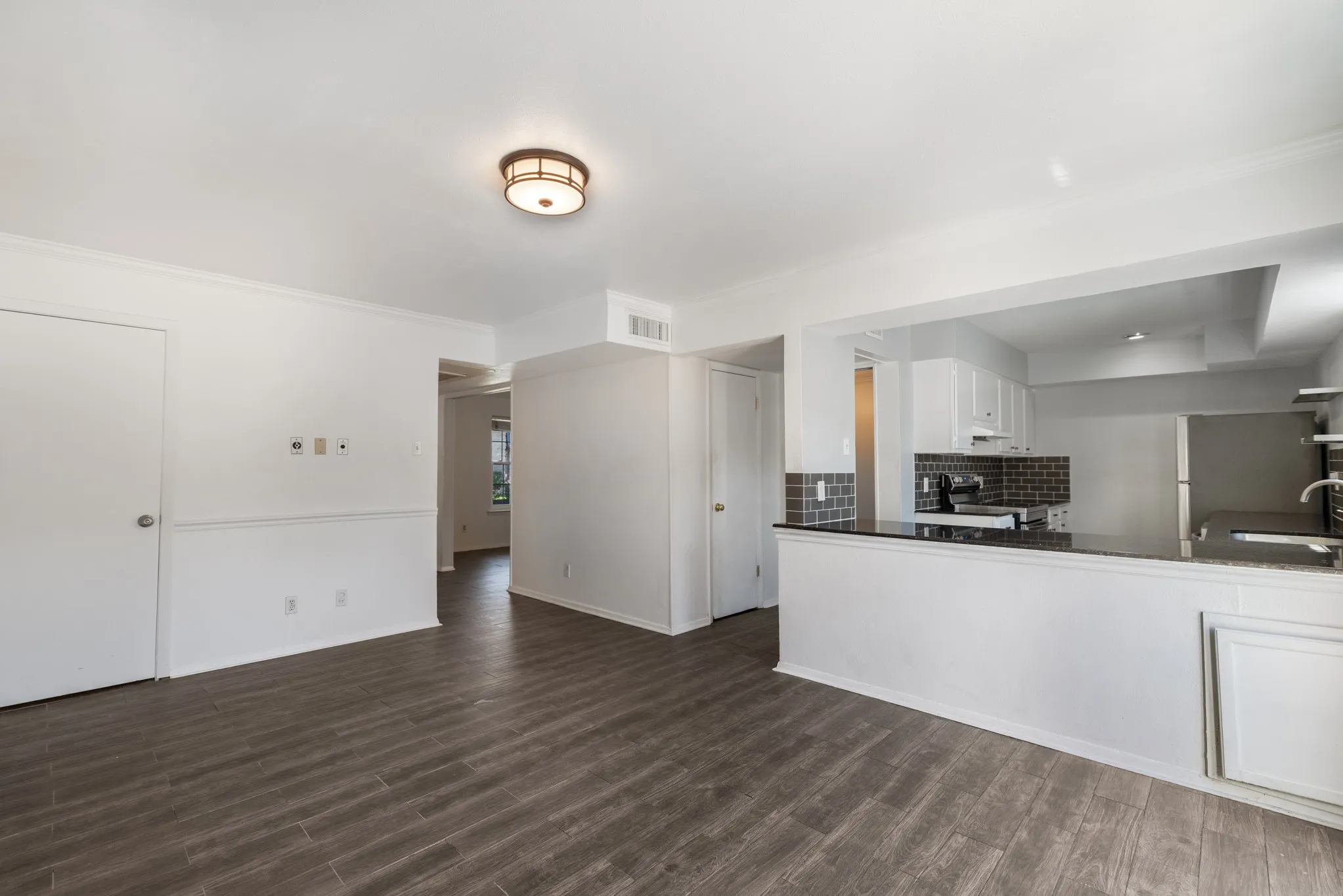 Wood-finish flooring, recessed lighting, crown molding, white kitchen cabinetry, and dark countertops
