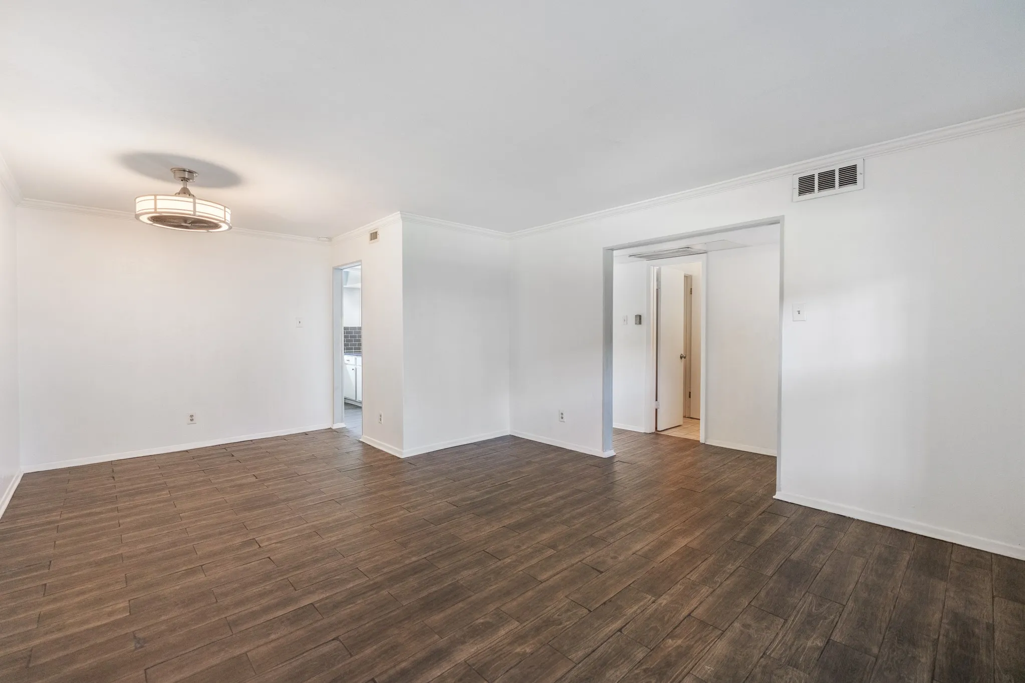 Wood-finish flooring, crown molding, archway, and overhead flush mount lighting