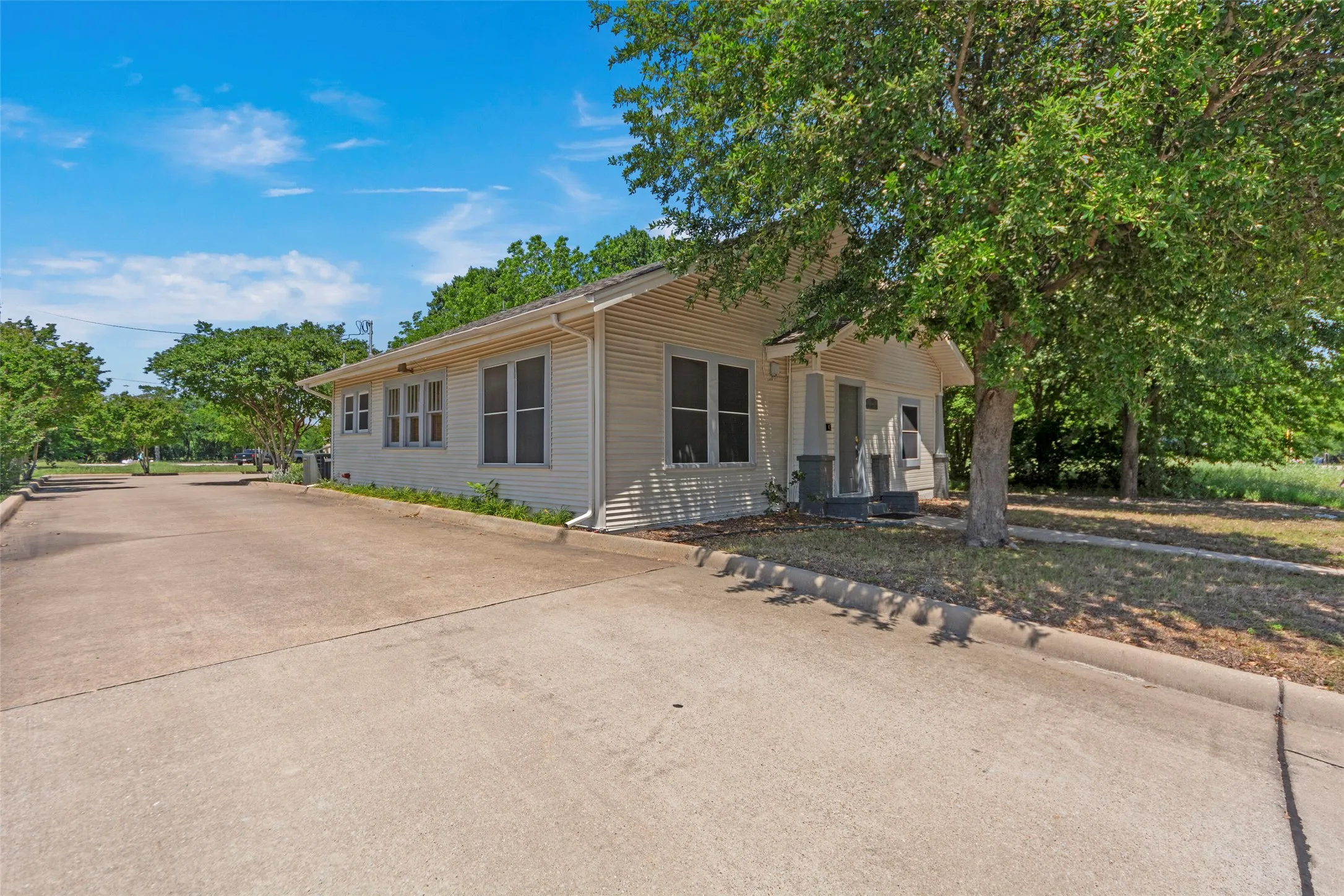 Siding exterior with multiple windows, covered porch entry, mature tree, and concrete driveway