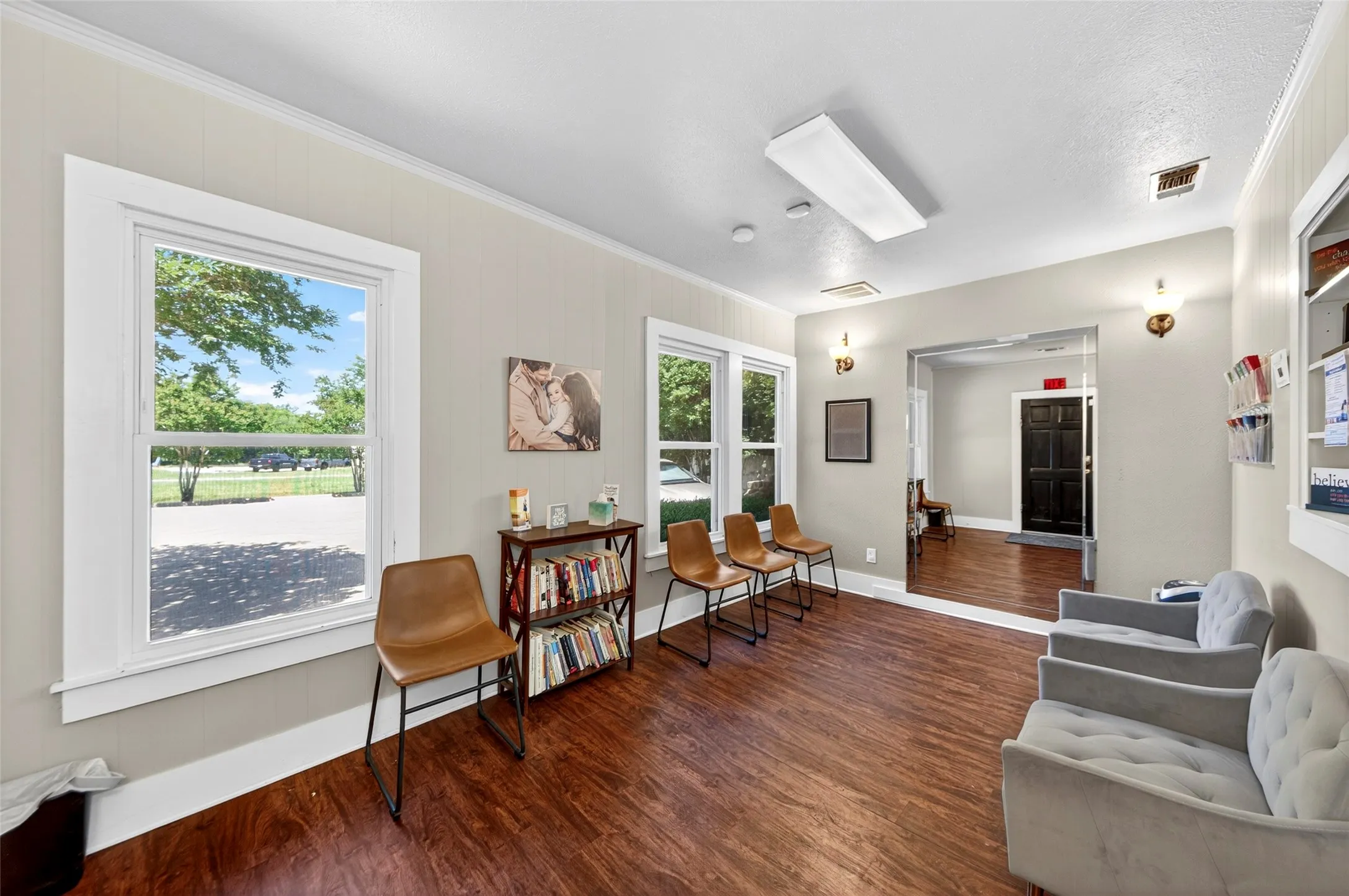 Wood-finish flooring, white trim, and light-toned wall paneling define this interior space, illuminated by multiple windows