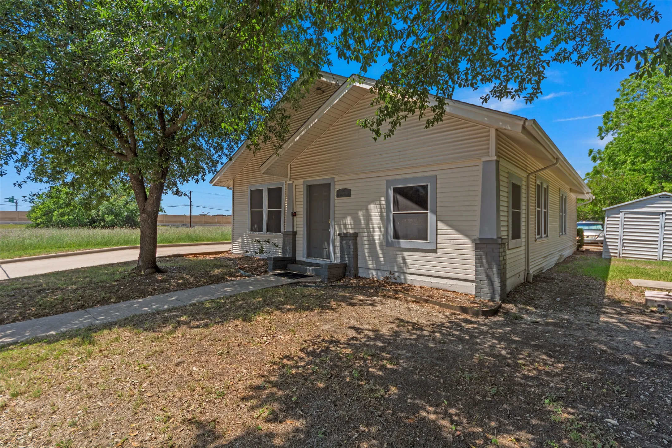 Siding exterior with a covered entry, concrete walkway, mature tree, and a detached storage shed